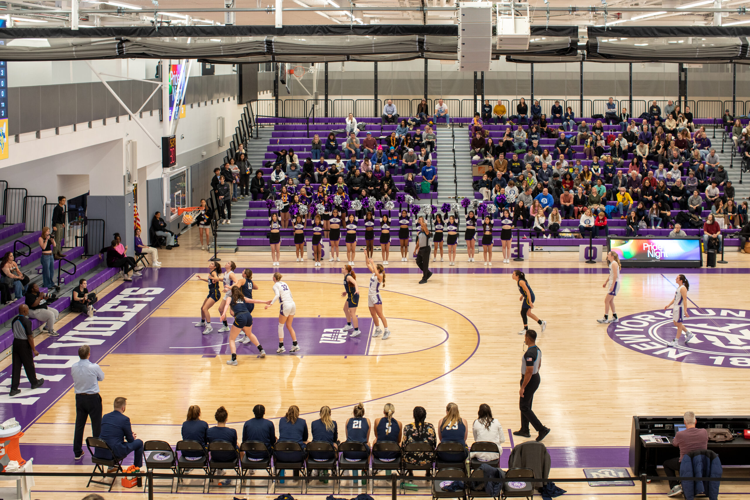 Two women’s basketball teams engage in a game on a court marked with NYU’s branding.