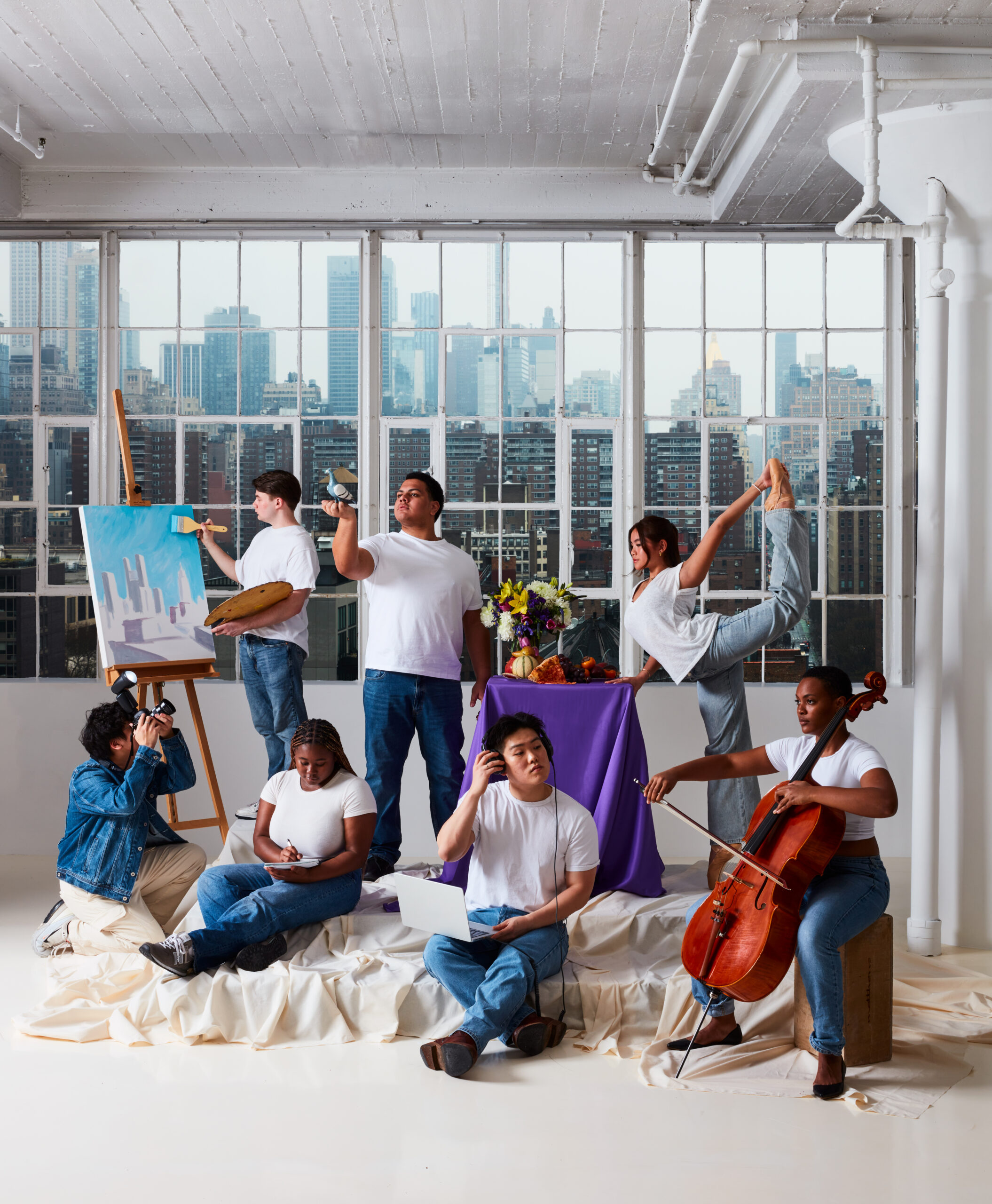A diverse group of seven people, dressed casually in white t-shirts and jeans, engage in various artistic activities such as painting, photography, writing, music, and dance in a bright studio with large windows overlooking a cityscape.
