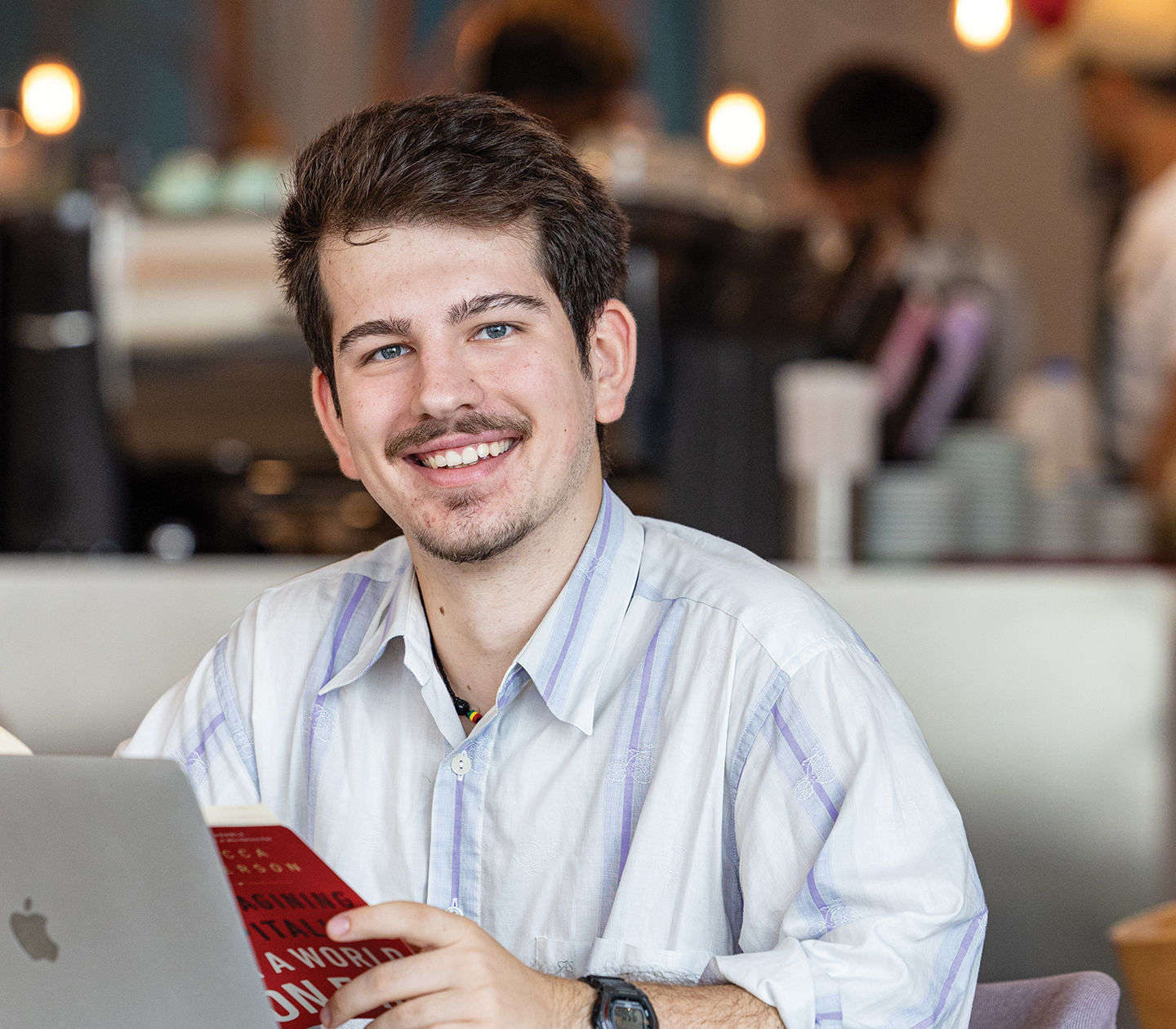 Stefan Mitikj, an NYU Abu Dhabi alum, sits in front of a laptop with a book in his hands.