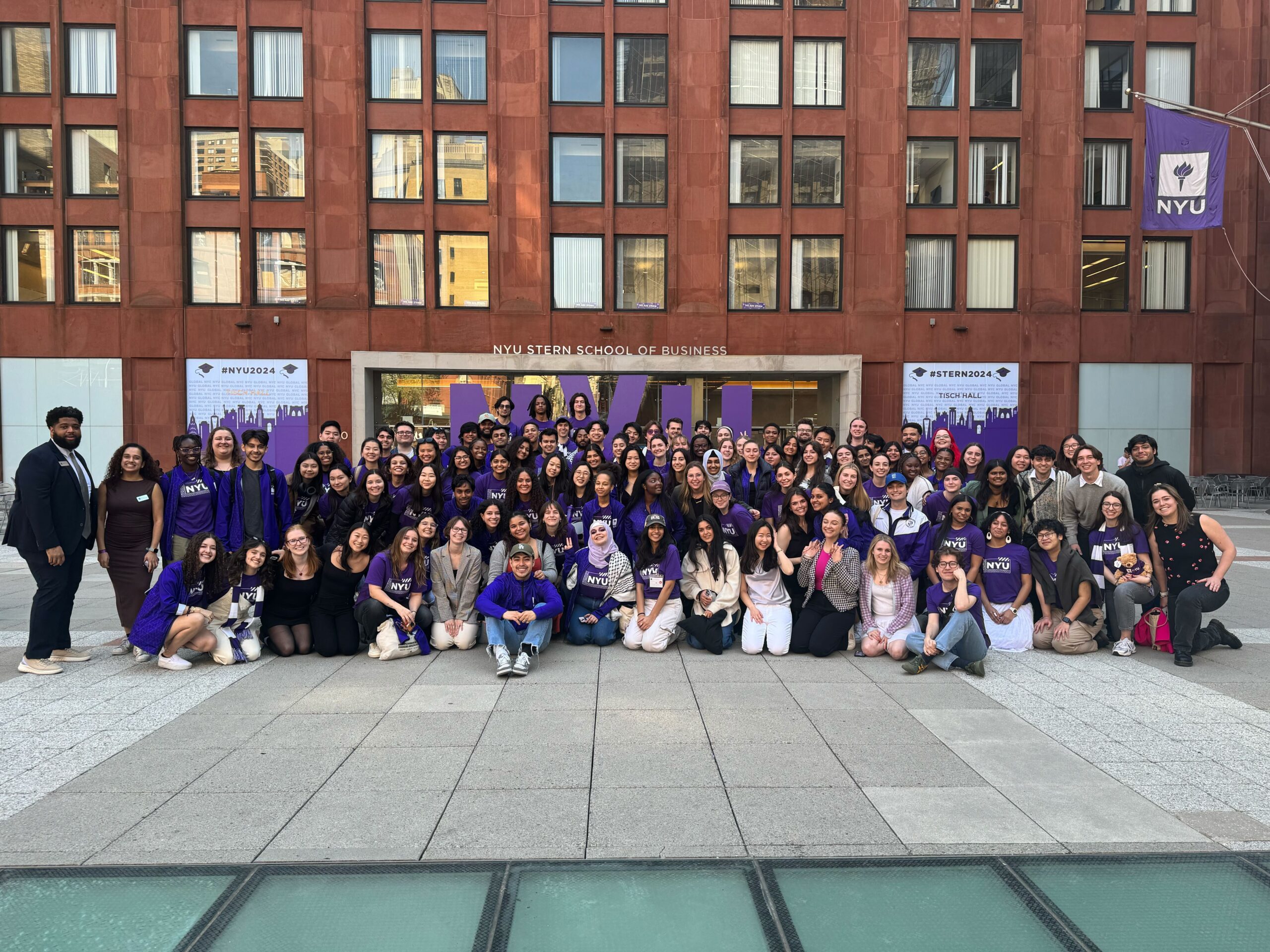 A large group of students posed in front of an NYU building.