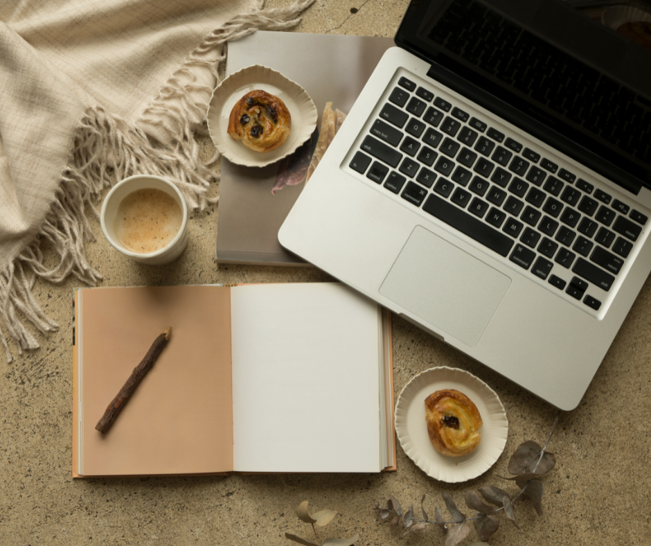 A photo of a computer, coffee, pastries and a notebook