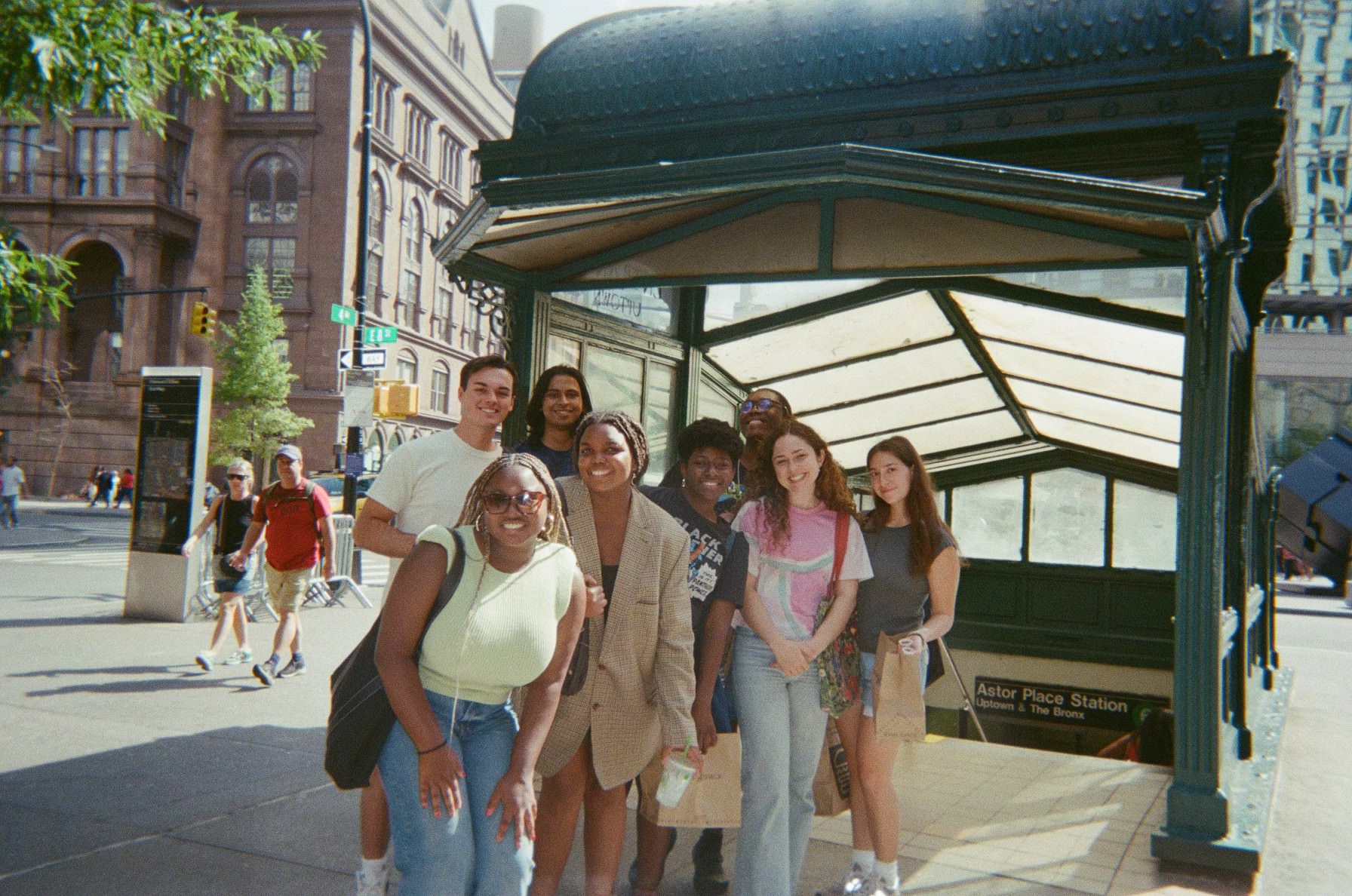 A group of students smiling in front of a subway station entrance.