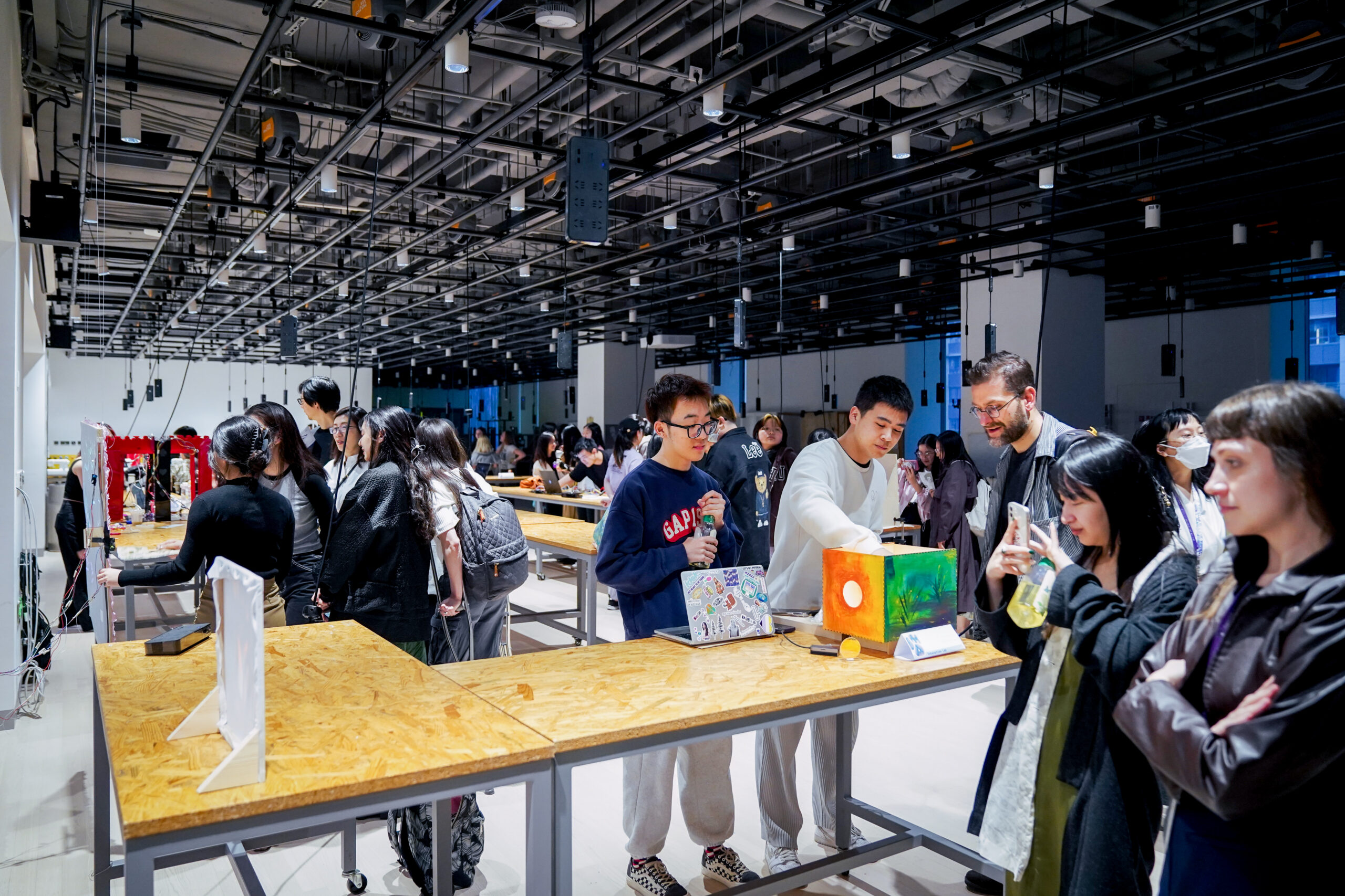 Students stand at a long fabrication table in the IMA