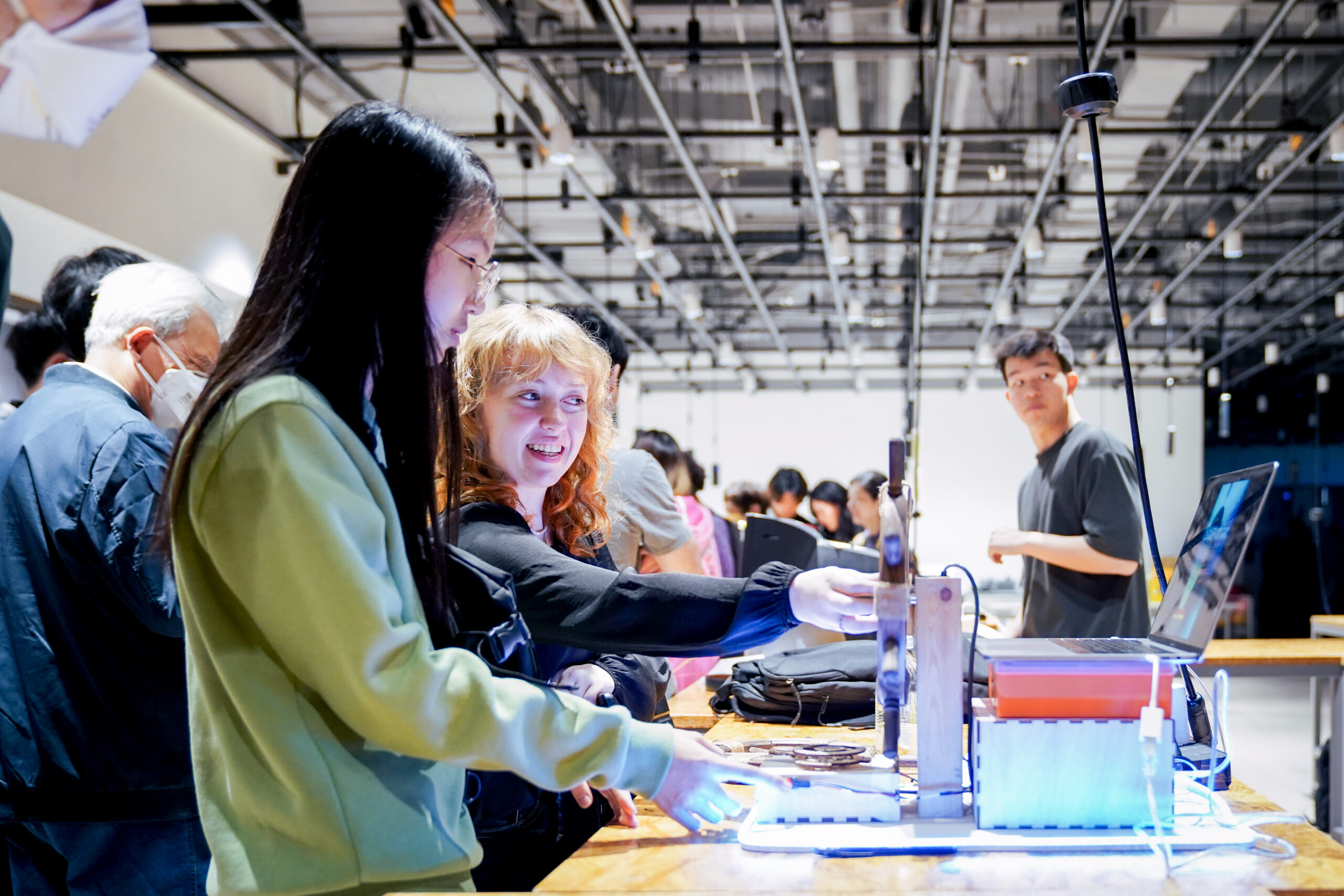 Students stand at a long fabrication table looking at computers in the IMA