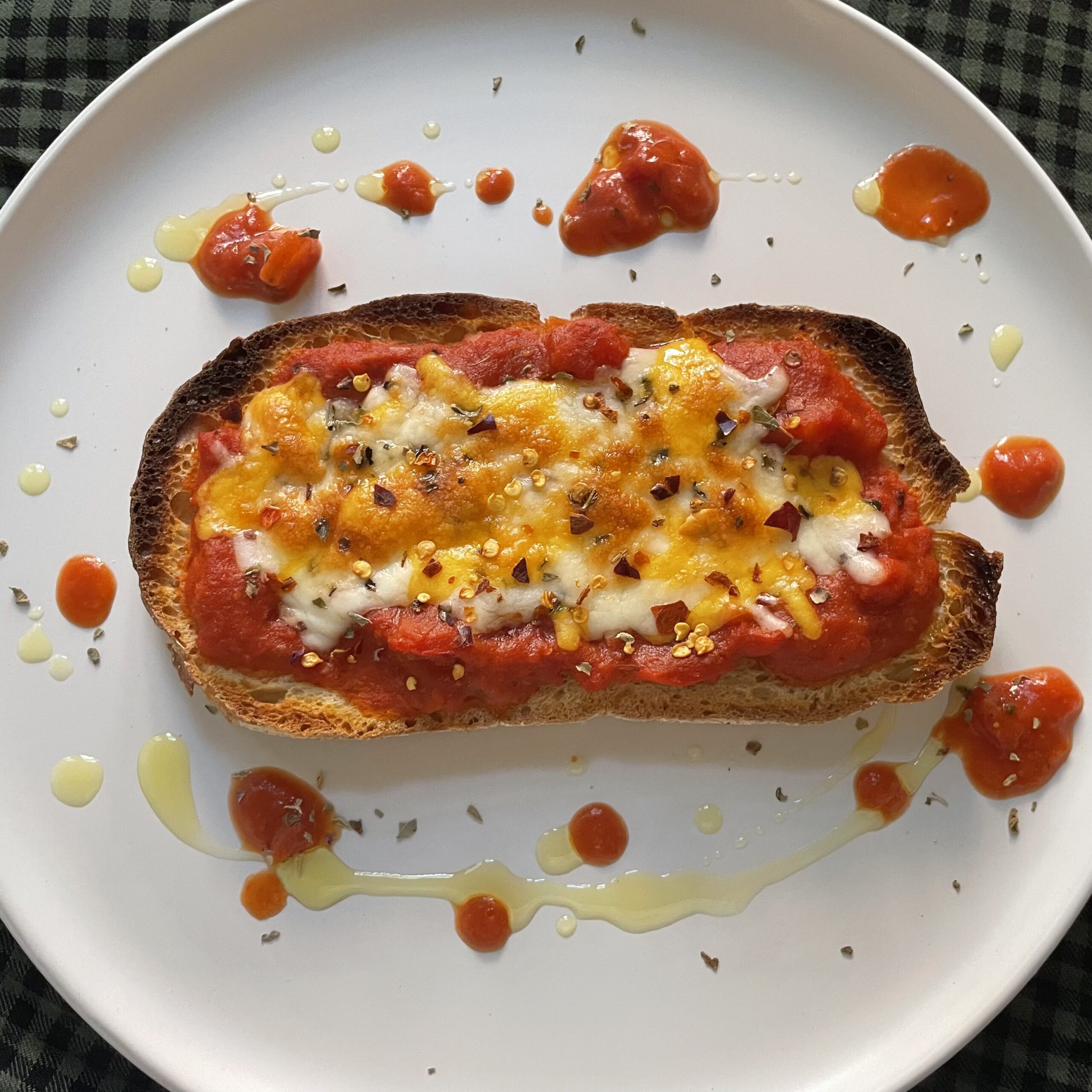 A white plate of toast with tomato sauce and melted cheese.
