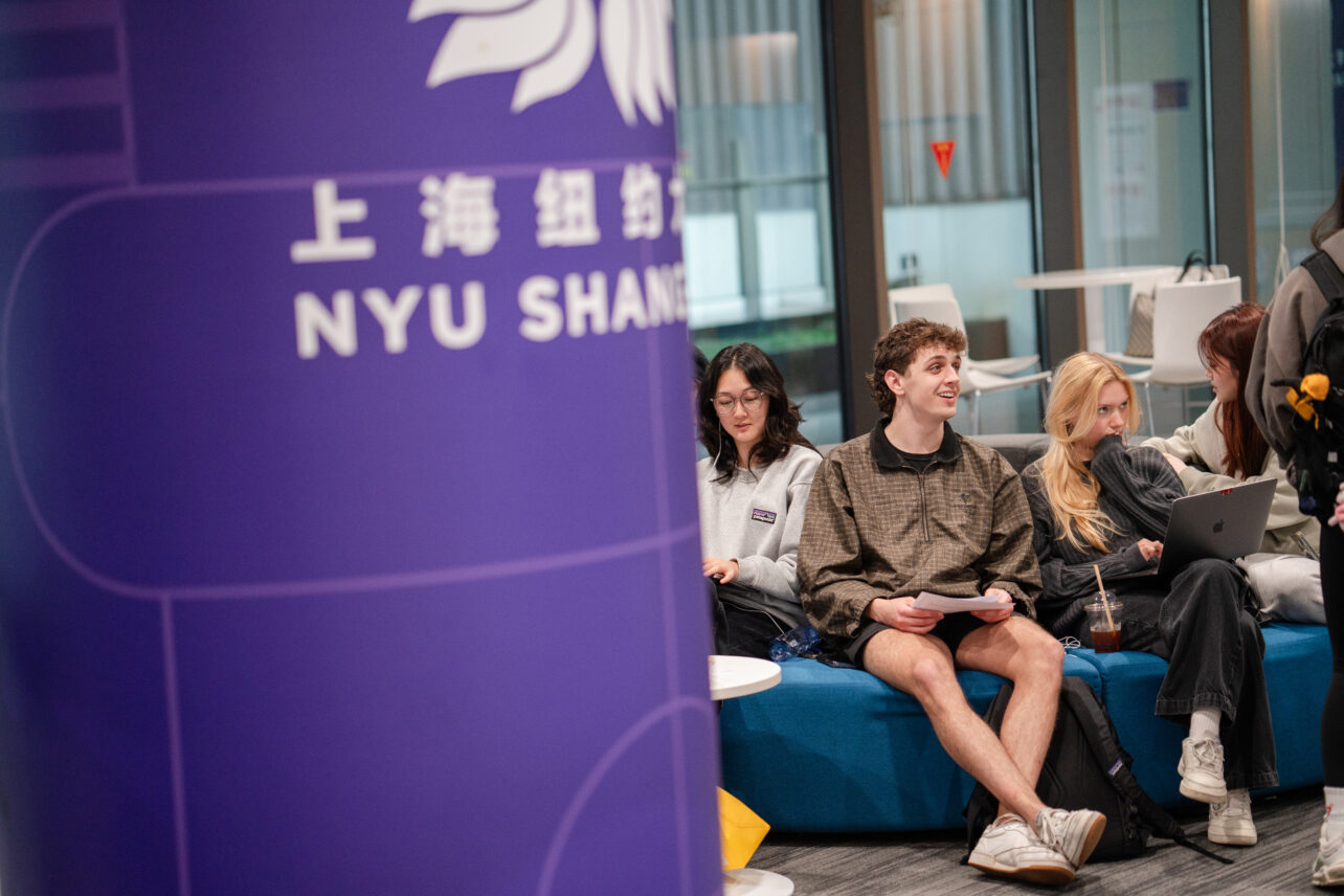 a NYUSH branded pillar and 3 students sitting beside it