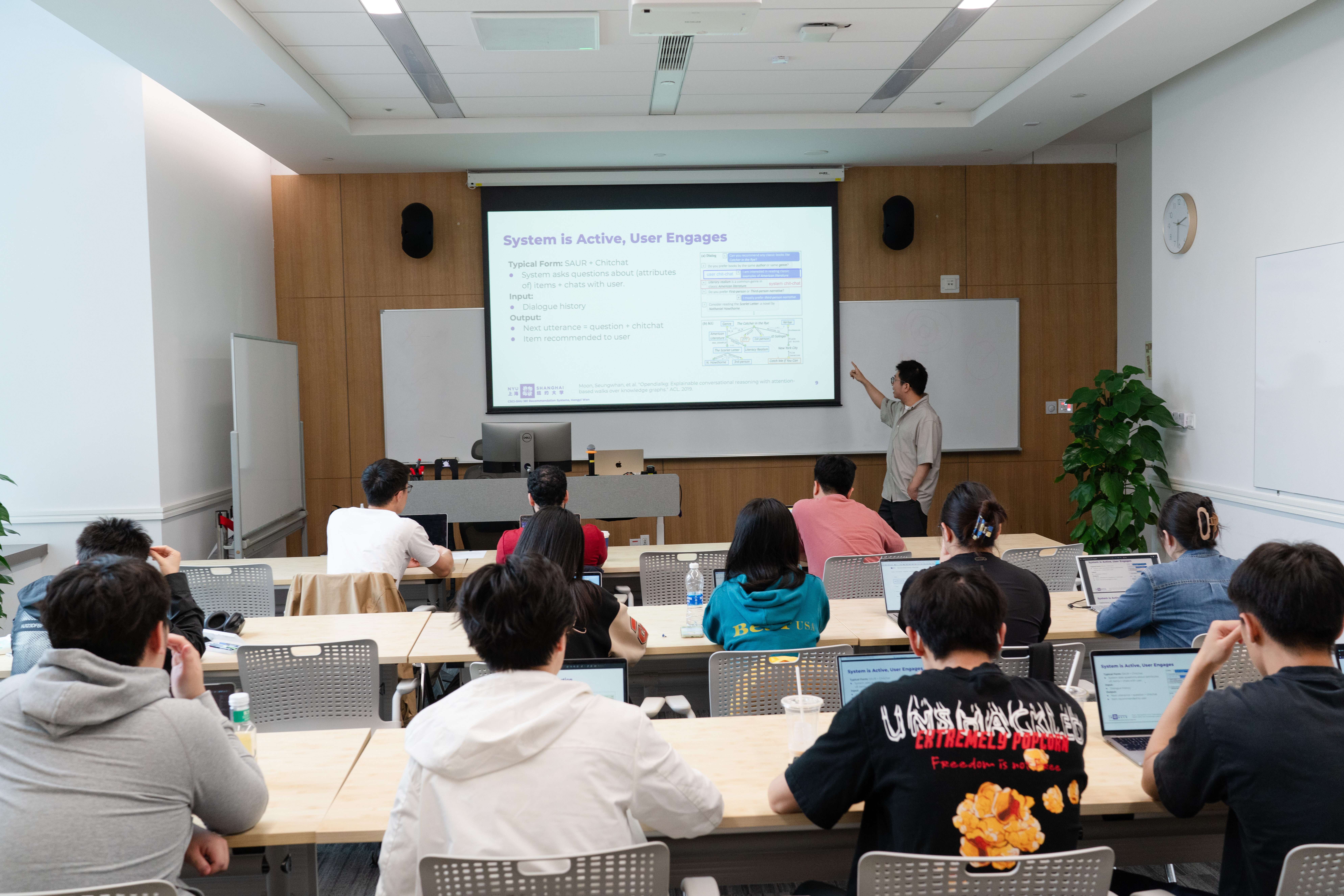 Students look at a professor teaching on a smart-screen