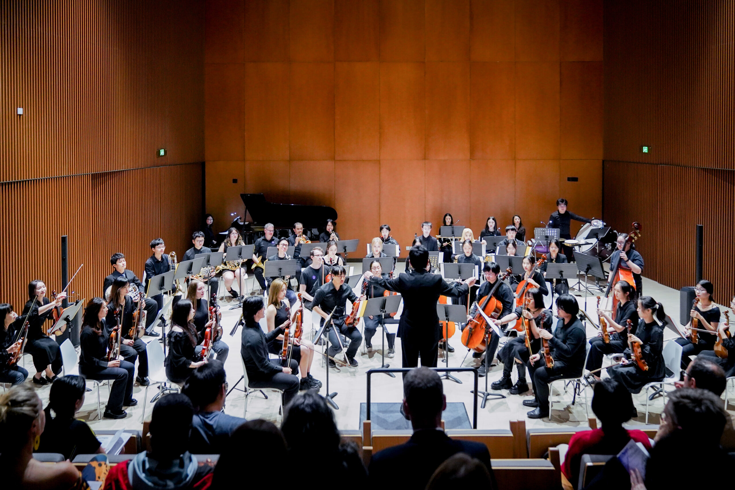 a conductor stands in front of an orchestra in the NYU Shanghai recital hall