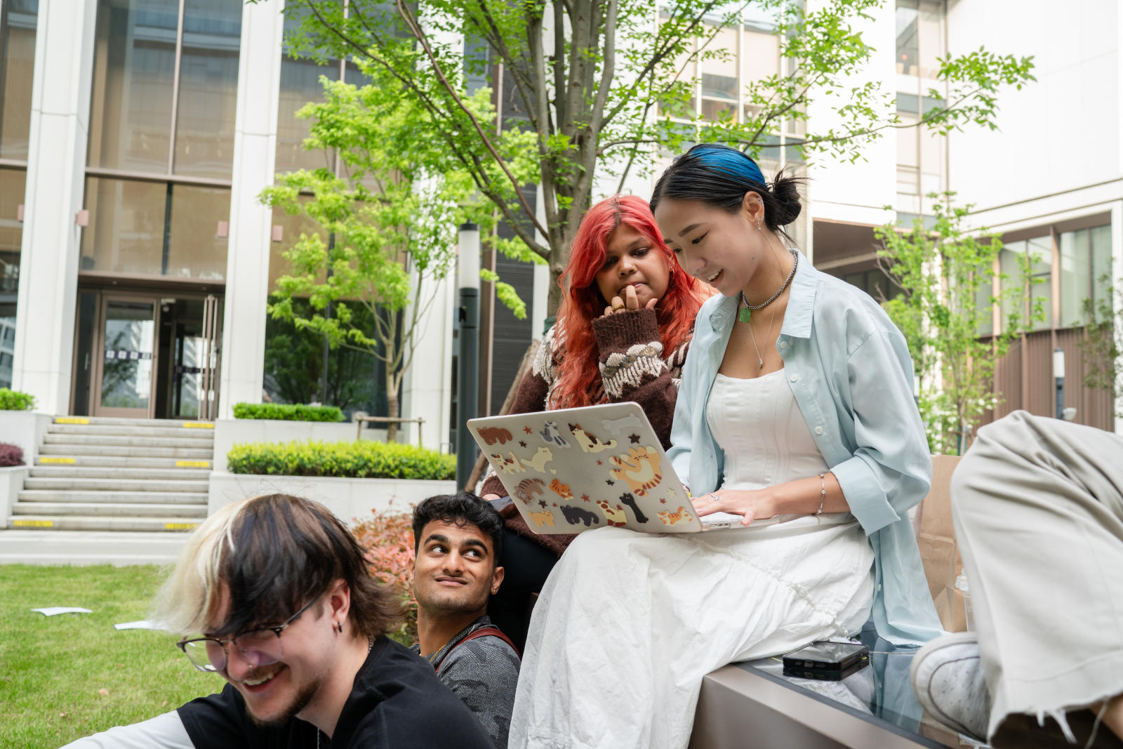 Four students have a conversation over their laptops in the NYUSH courtyard