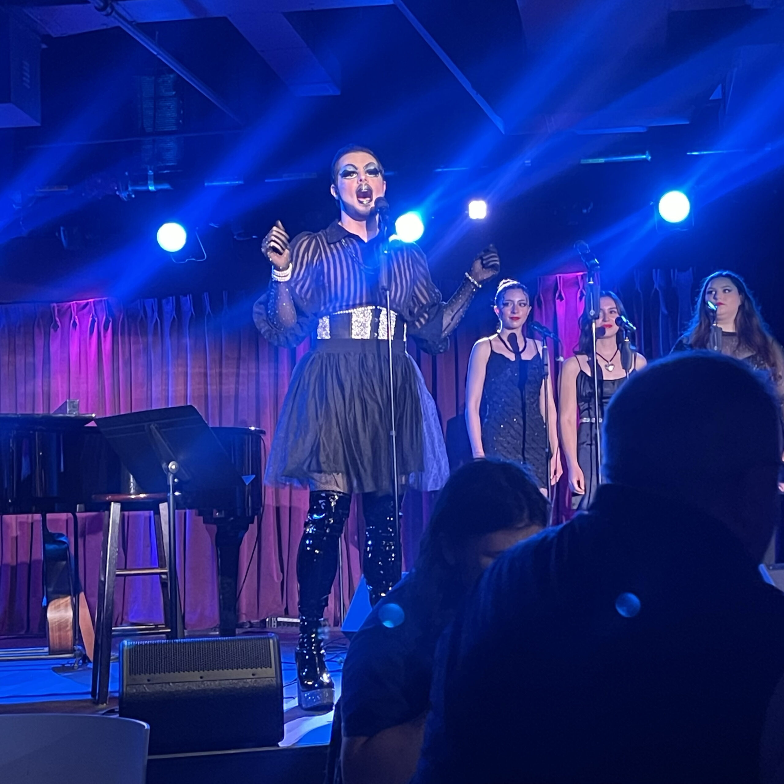 NYU student Toby as Toast sings onstage with a microphone. He is accompanied by three backup singers.