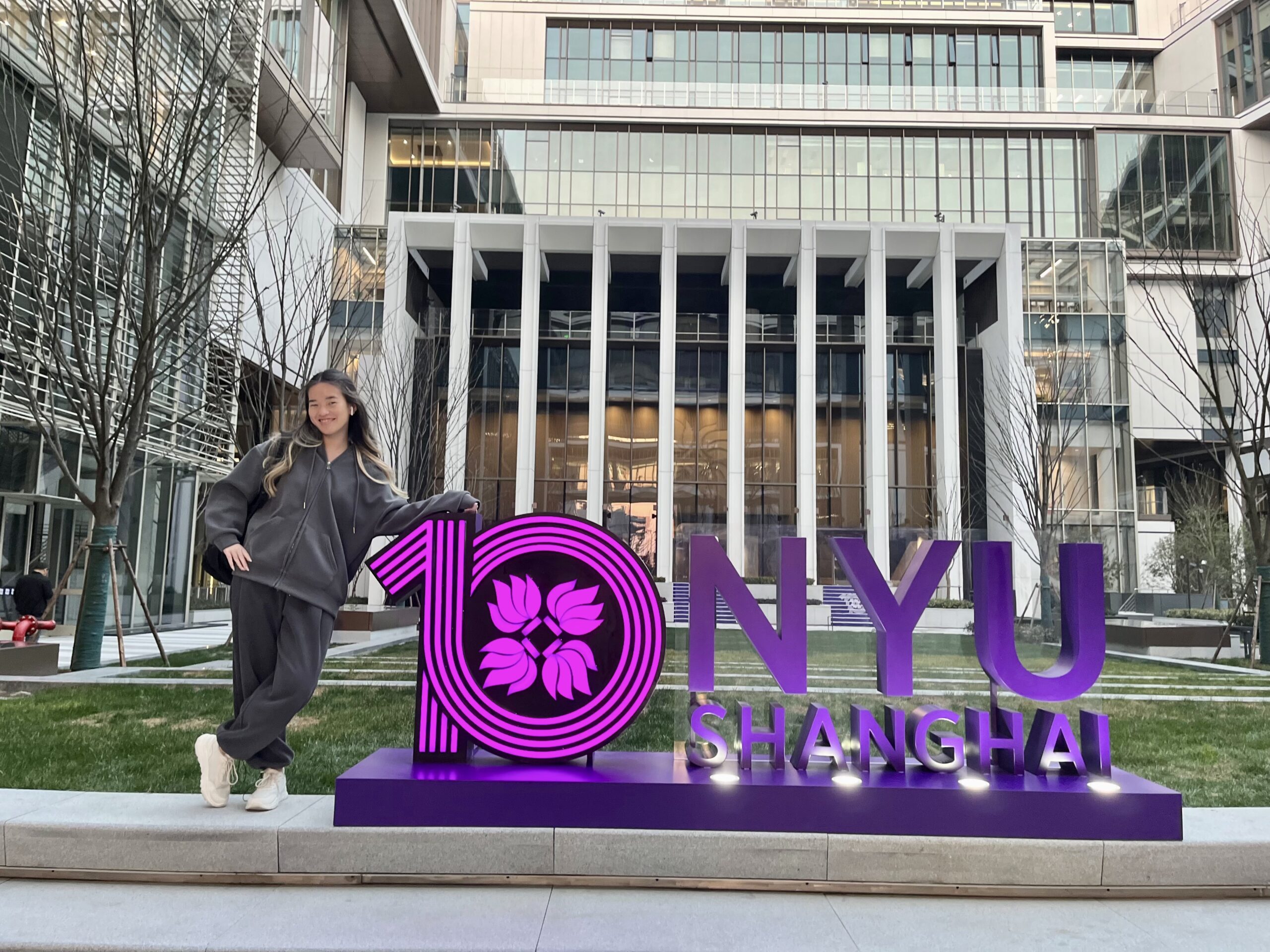 Leyla posing next to a large sign that reads “10 NYU Shanghai” on the NYU Shanghai campus