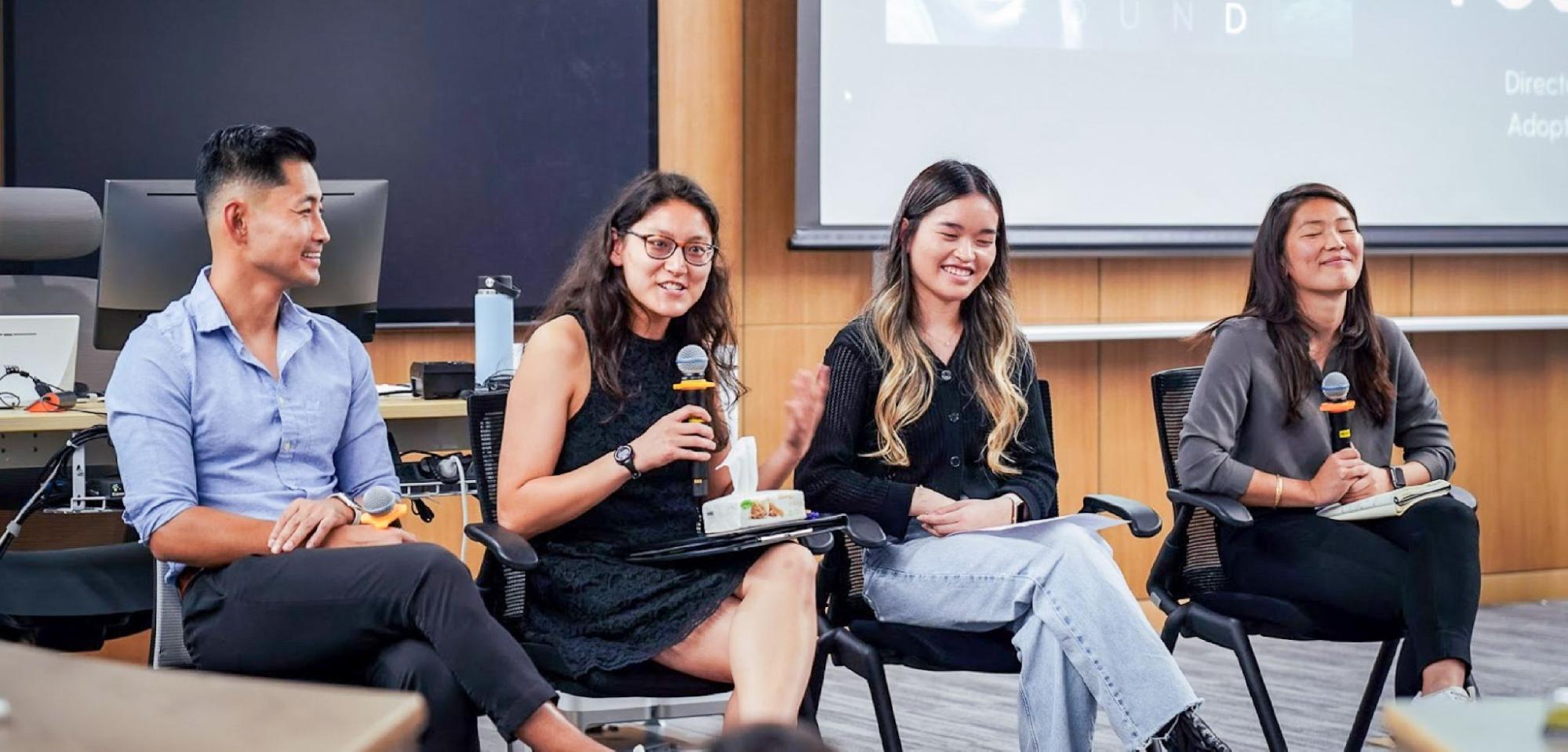 Adoptee panel members and event organizers smile as they are seated in front of an audience.