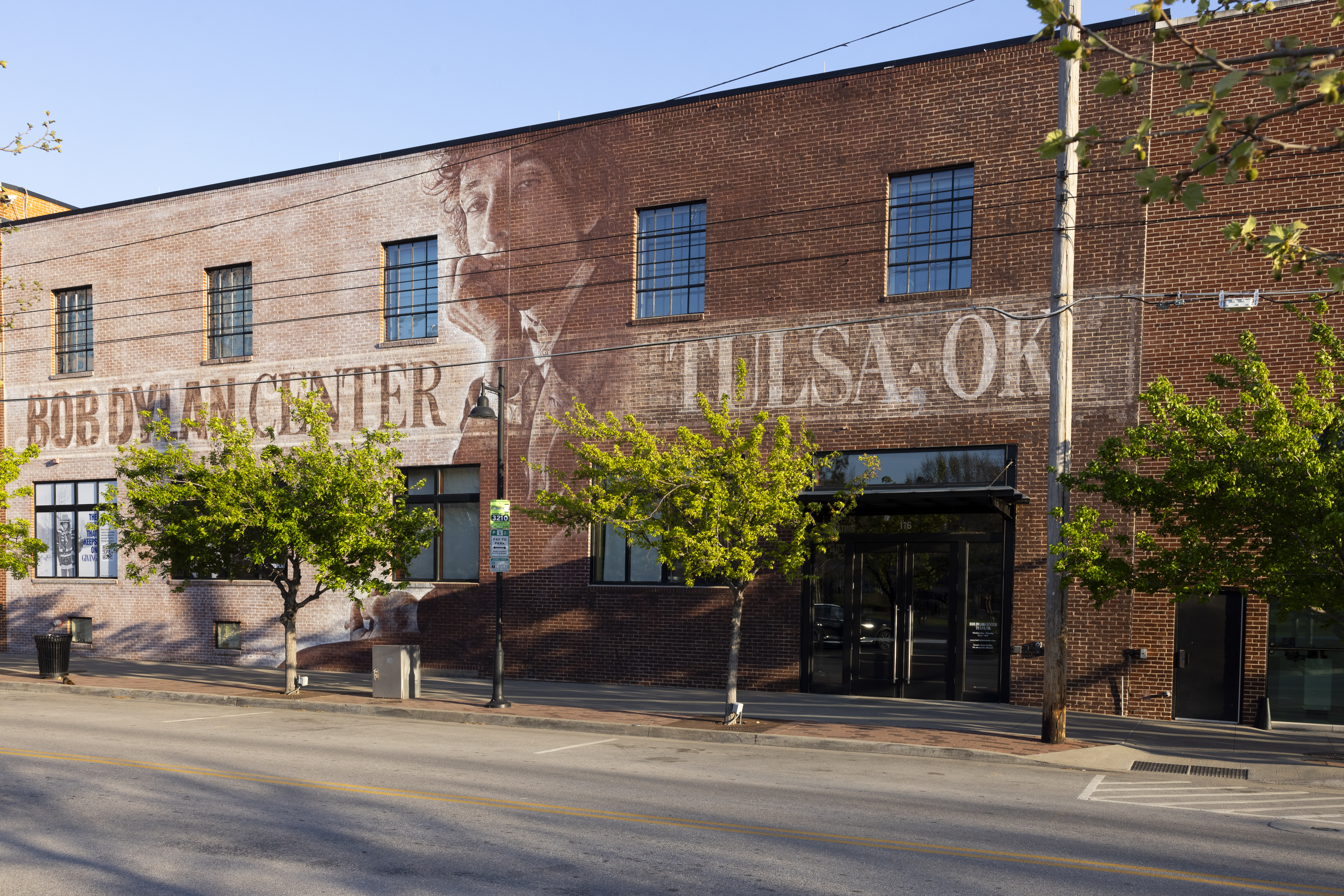 A brick building features a large mural of Bob Dylan with the text 