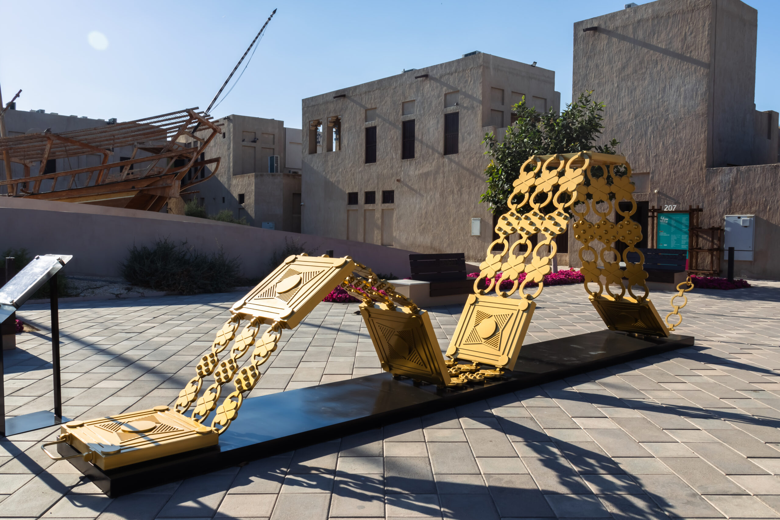 A modern outdoor sculpture featuring interconnected golden panels is displayed on a paved area.