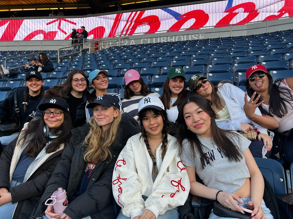 A group of girls sits together and smiles at a baseball game.