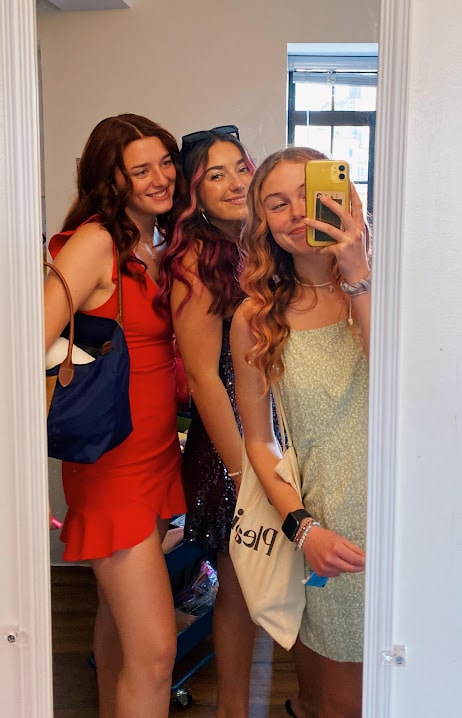 Three girls in dresses pose for a mirror photo.