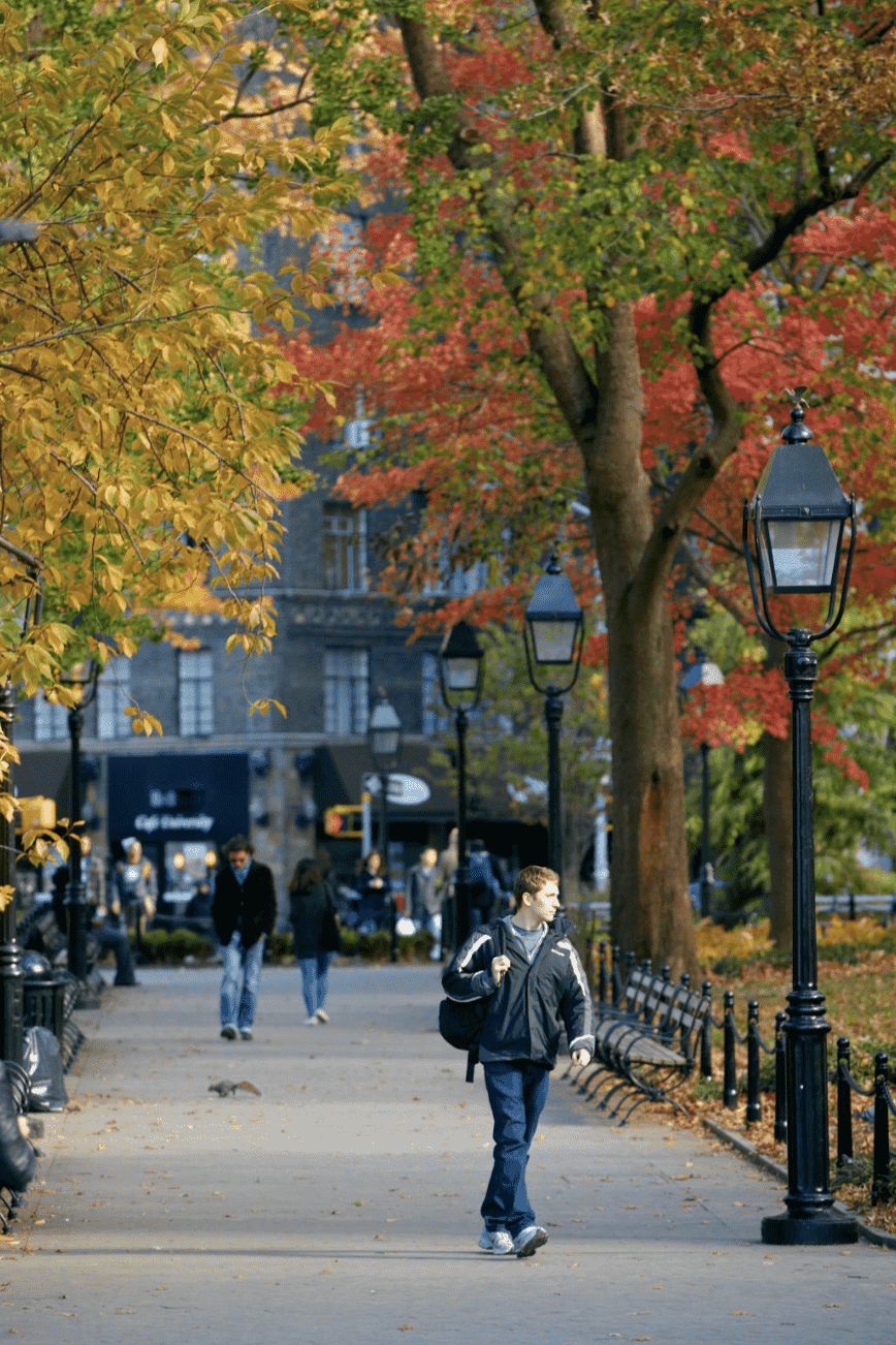 A student walking through NYU's campus during the fall