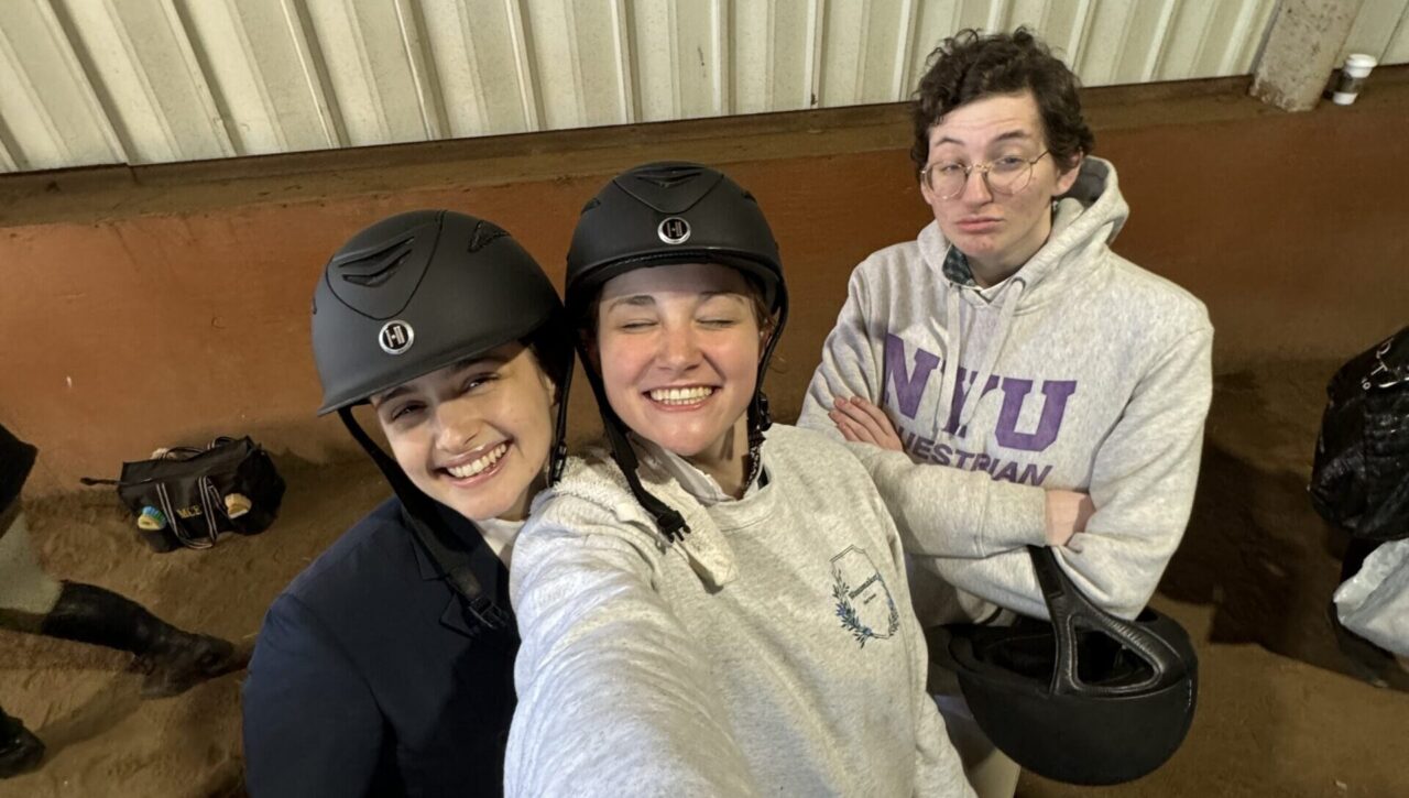 3 riders smile at the camera while wearing their NYU Equestrian gear