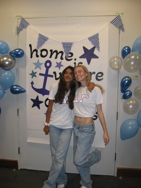 Two girls posing in matching shirts in front of a sorority banner.