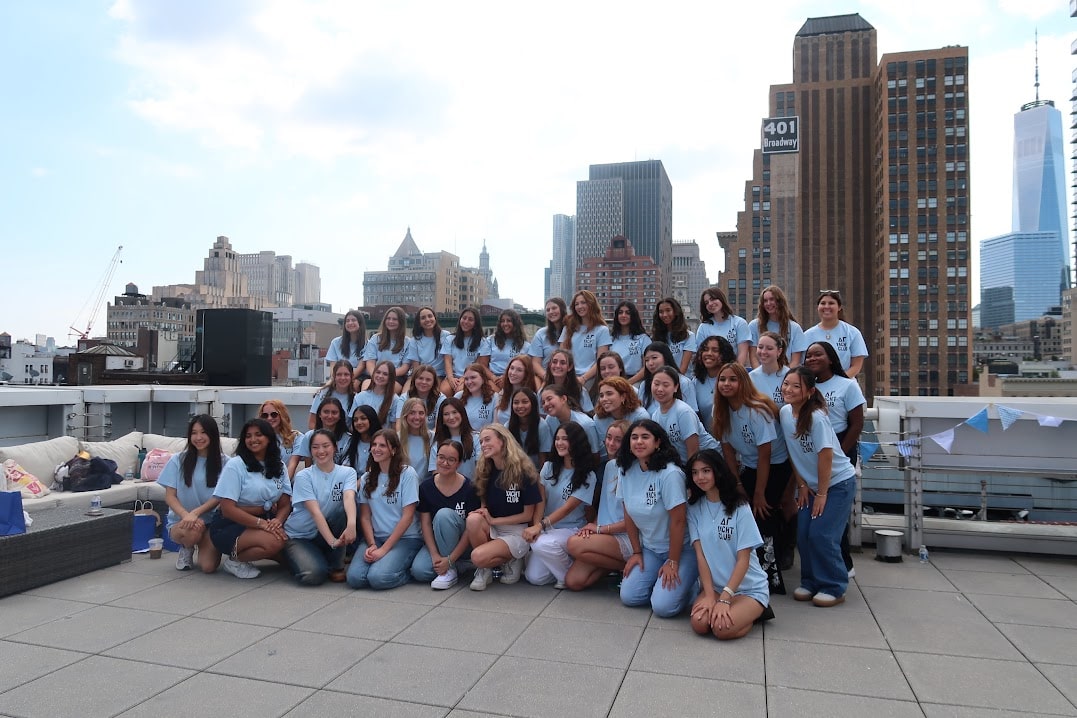 A big group of girls smiling on a rooftop venue with NYC skyline views.