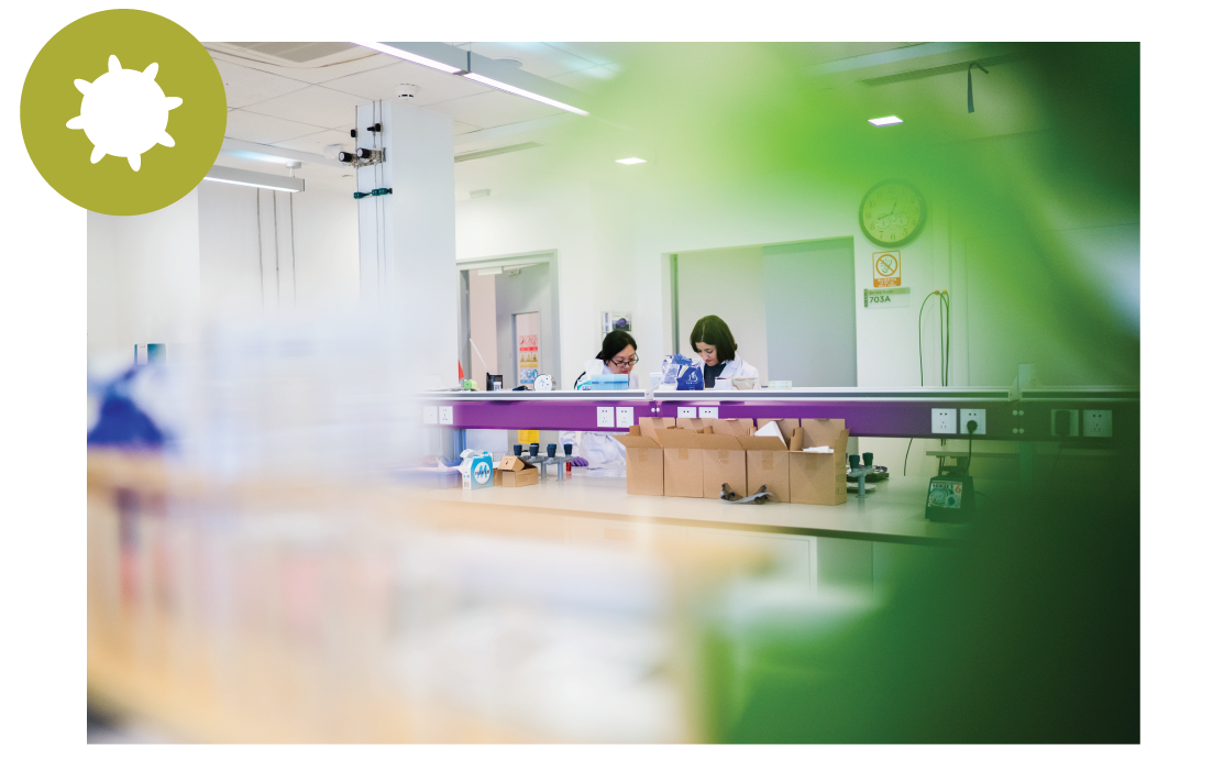 Students working in a lab, with a green circle containing a graphic of a germ in the upper left corner of the image.