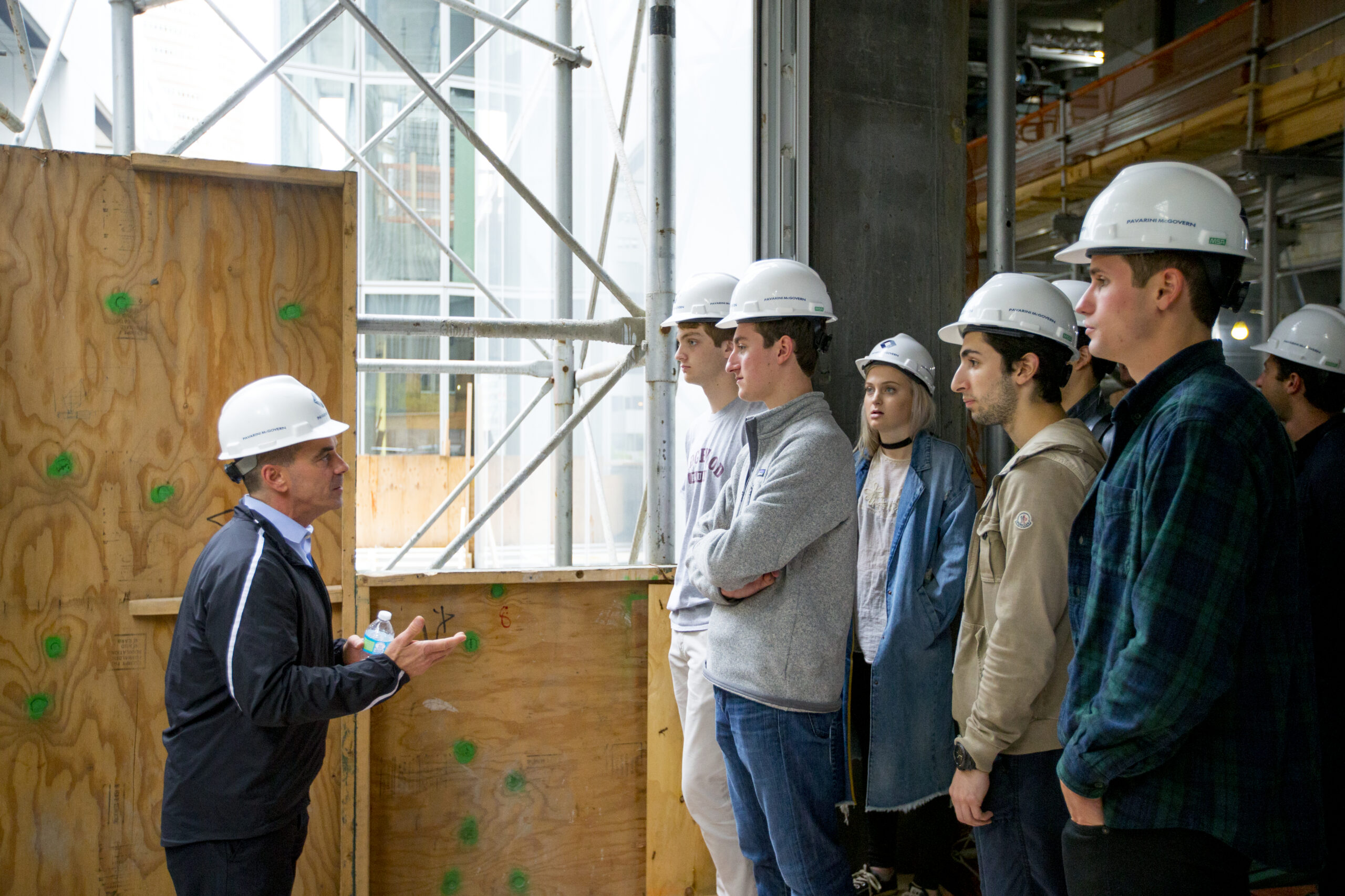 A group of students wearing hard hats and listening to a guide during a site tour.