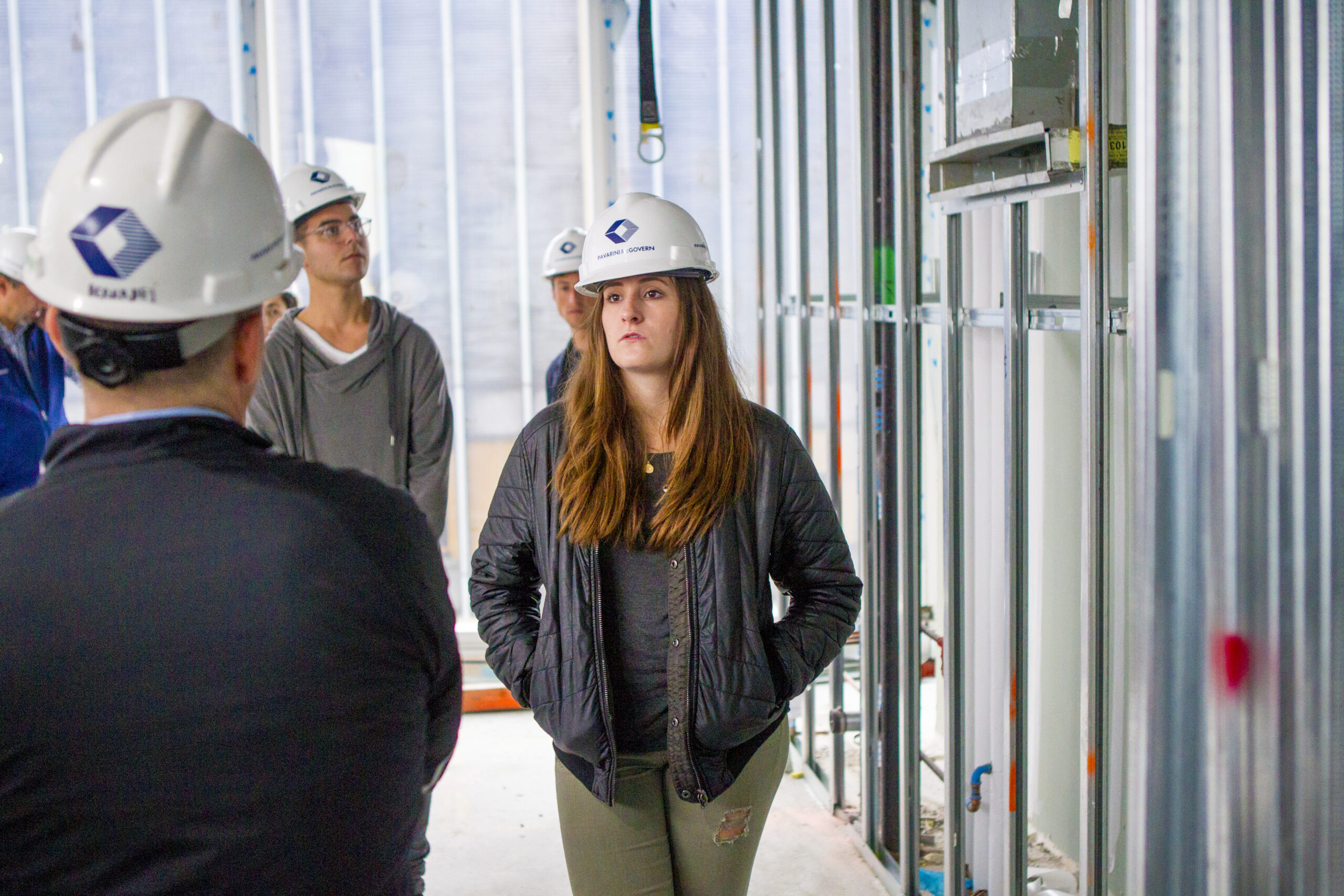 A student wearing a hard hat, talking to a professor in a class tour of a construction site.