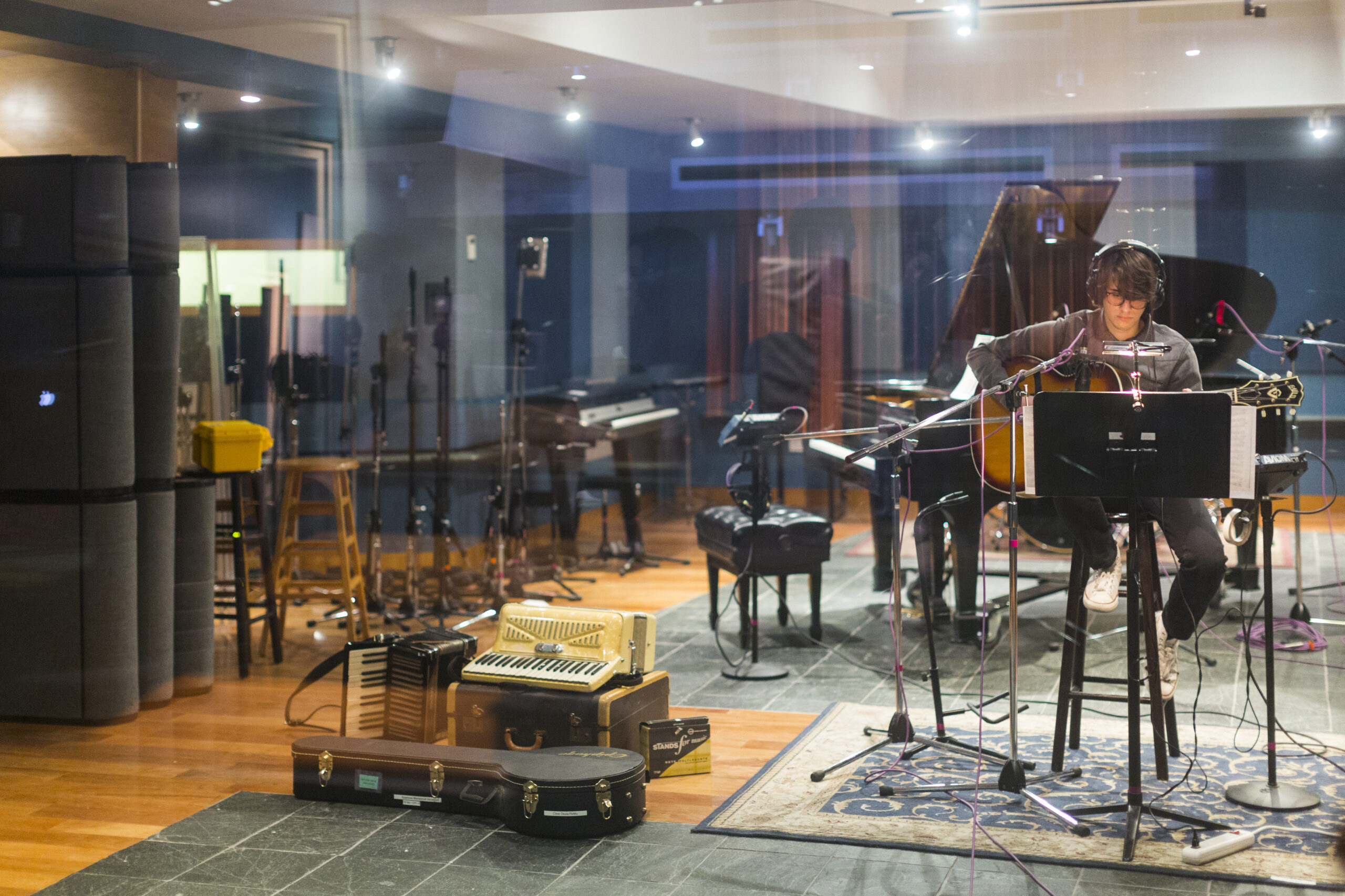 A student playing guitar in a recording booth.