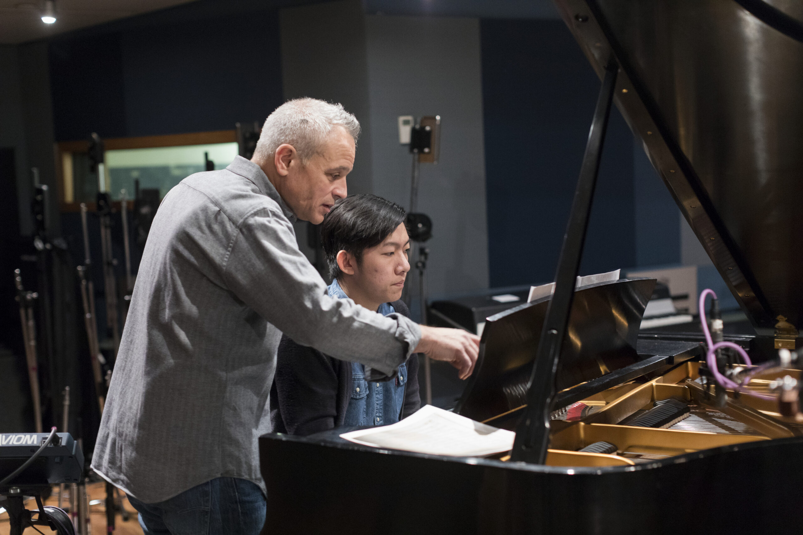 A professor assisting a student on the piano.