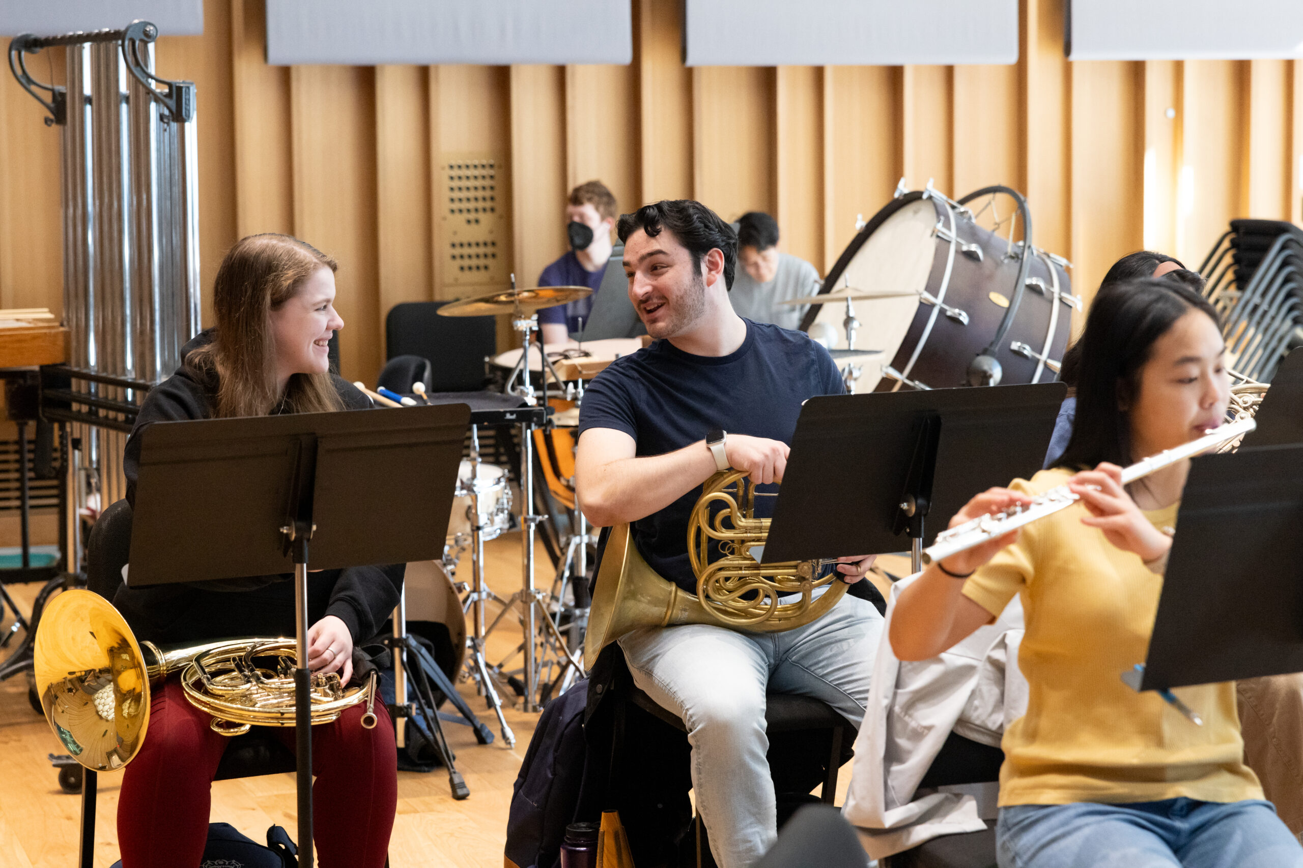 Two students talking in an orchestra class while holding their instruments.