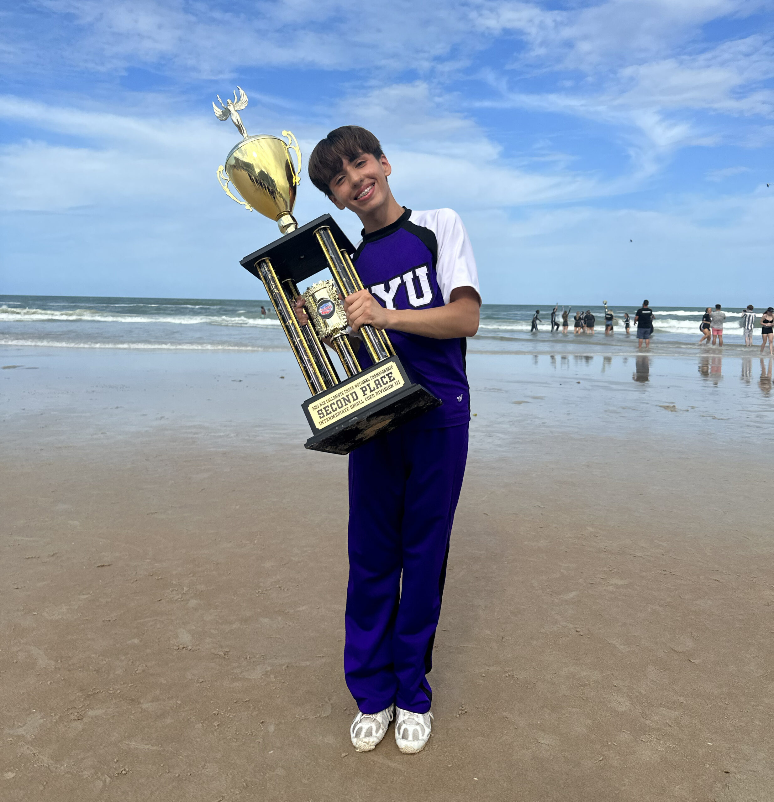 Isaac Garcia holds a trophy on a beach.