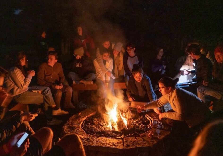 Student sit around a campfire.