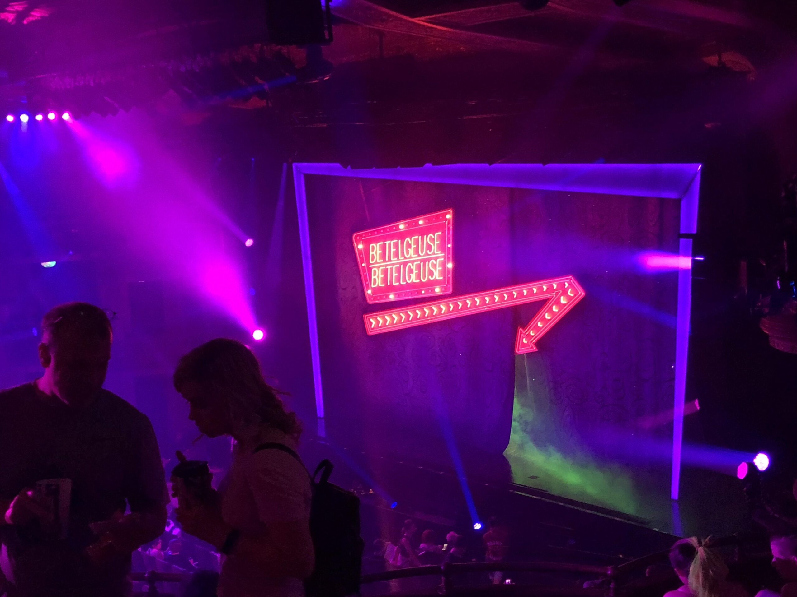 Neon lights and beams outside the vibrant and eccentric curtain of a Broadway theatre.