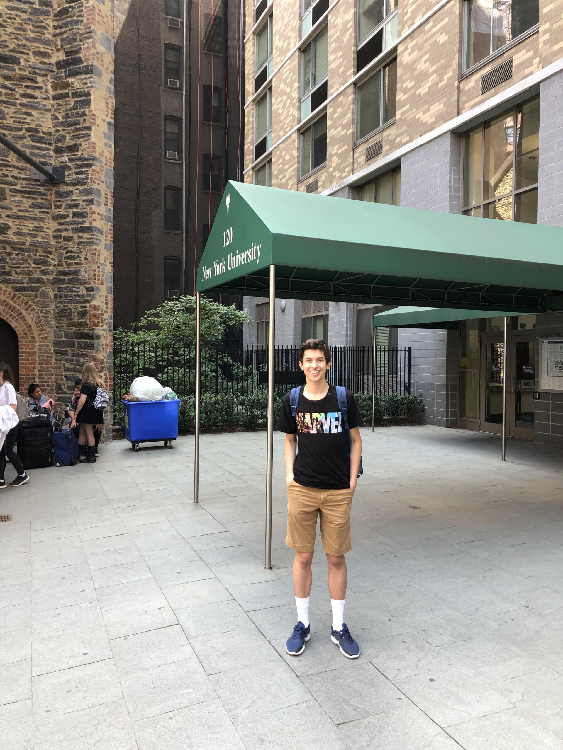 A teenager smiles in front of a residence hall where Tisch Summer High School Program students live for the summer.