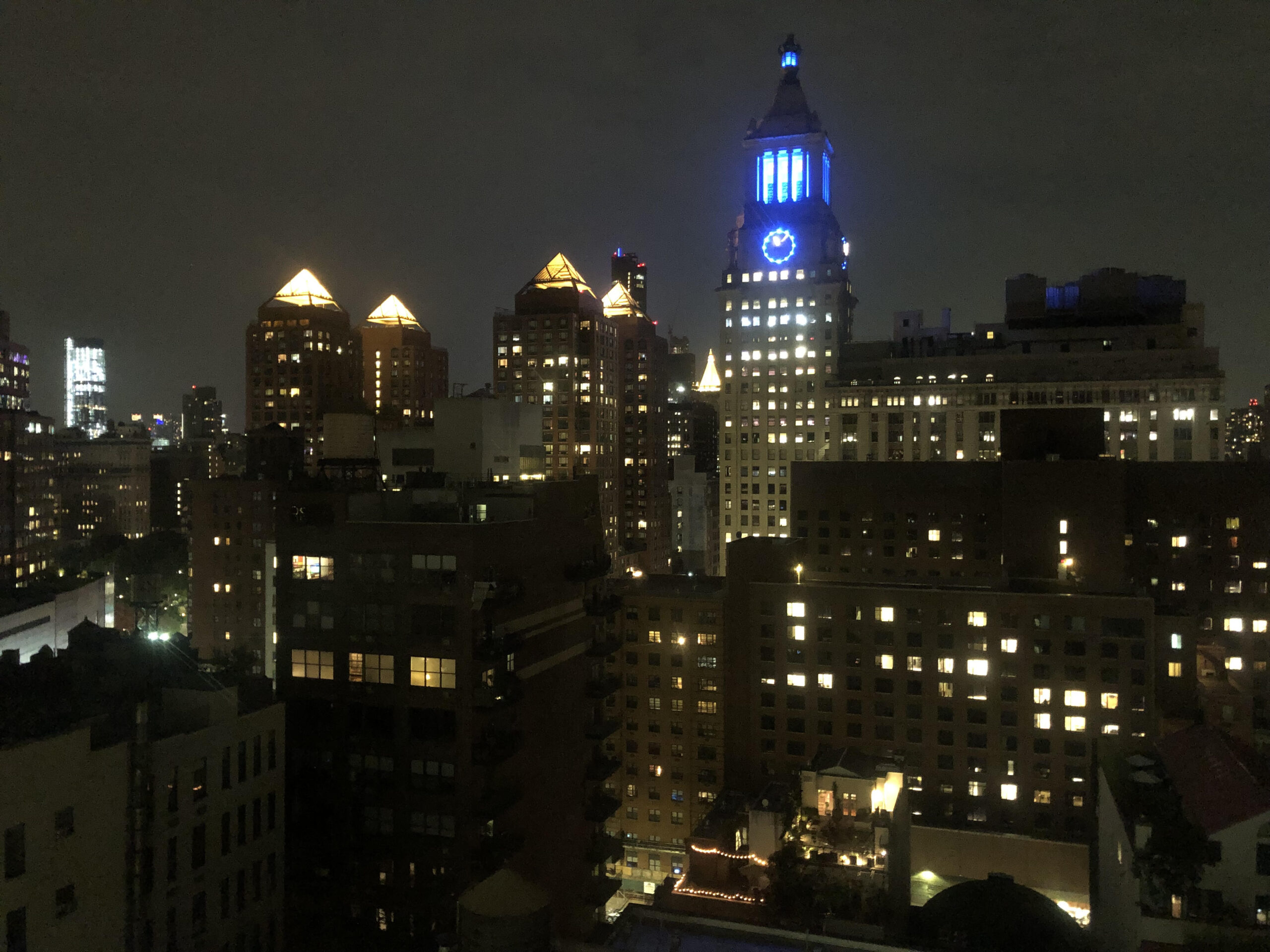 The New York City skyline lit up at night, including a clock tower with neon blue lighting. This was my view during the program.