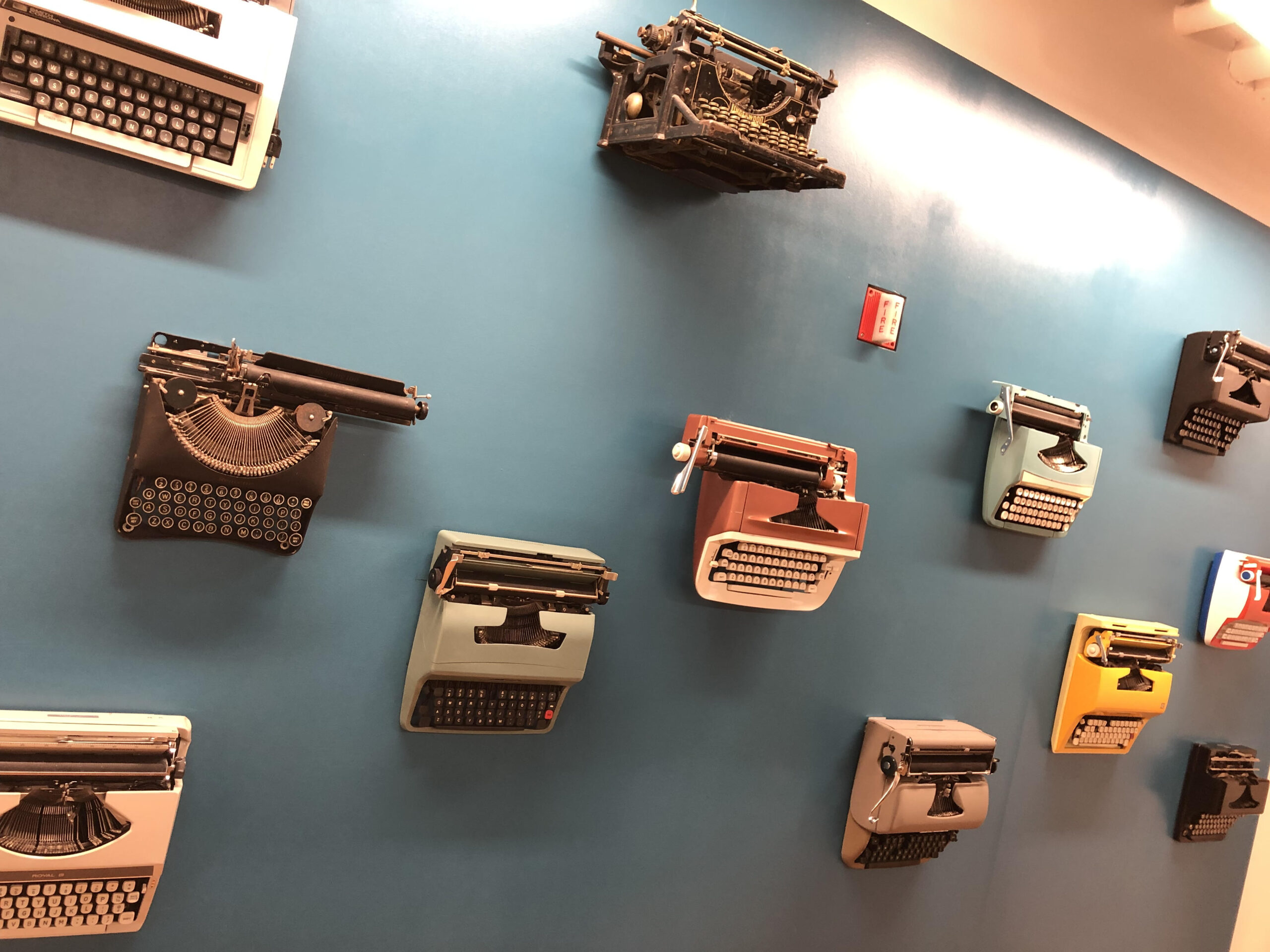 A series of typewriters of varying color, make, and model, hang on a blue wall. This is where I took classes throughout the duration of the program.