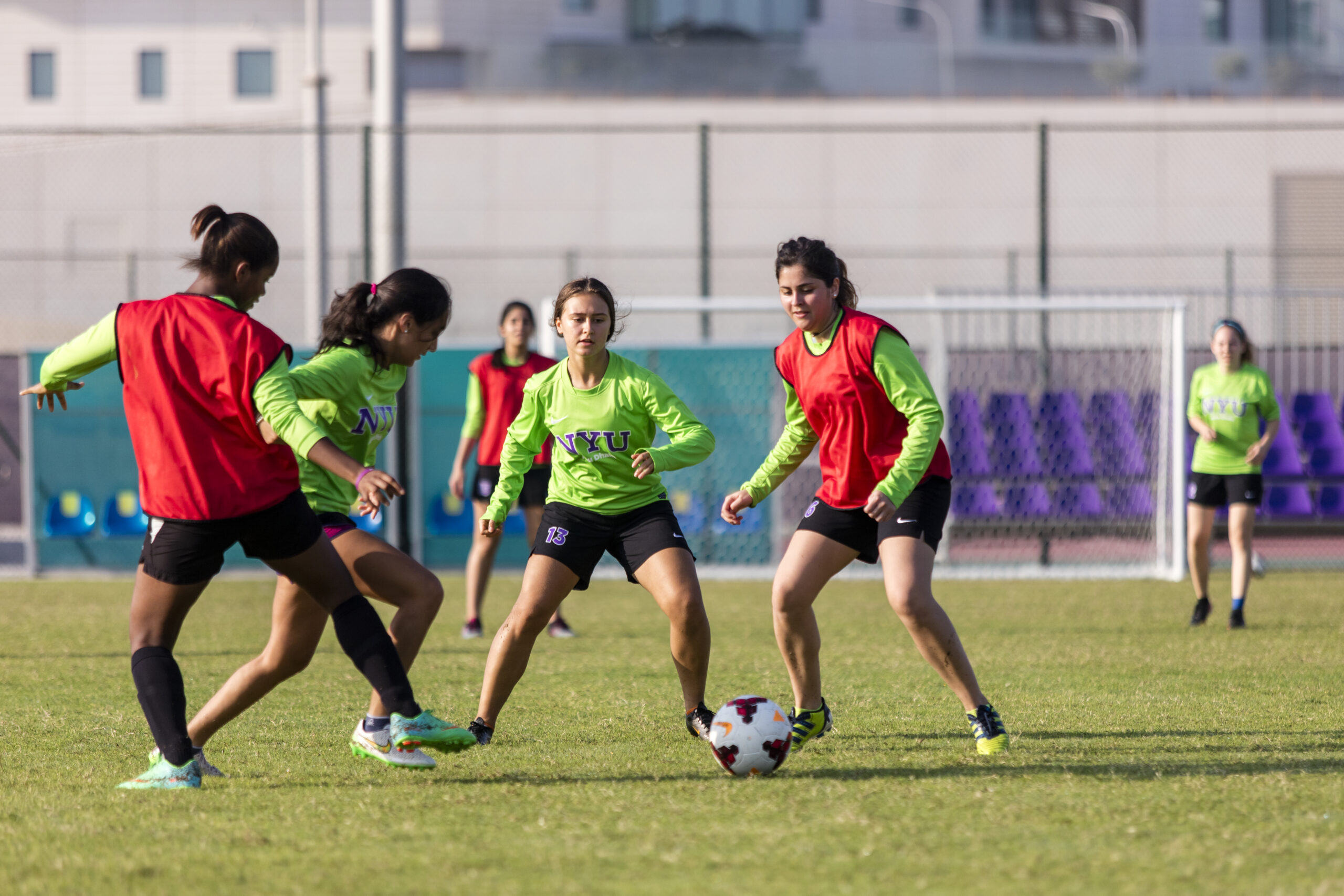 Women soccer players wearing green and red jerseys compete for the ball during a soccer game on a grass field.