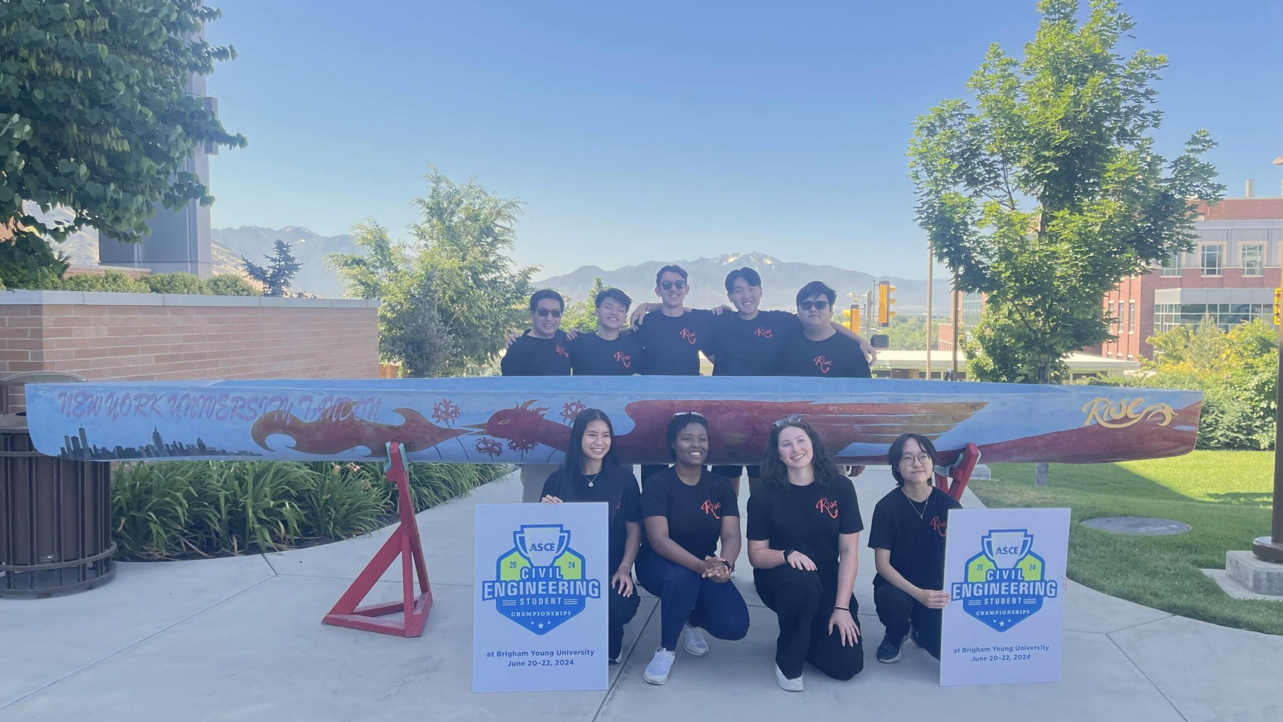 Nine people wearing matching black shirts pose with a decorated concrete canoe featuring a red dragon, 