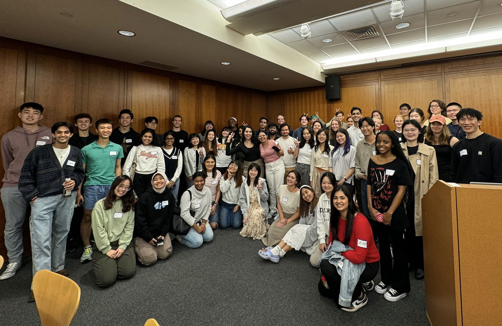 A group of students in a classroom or meeting room with wooden paneling pose for a photo.