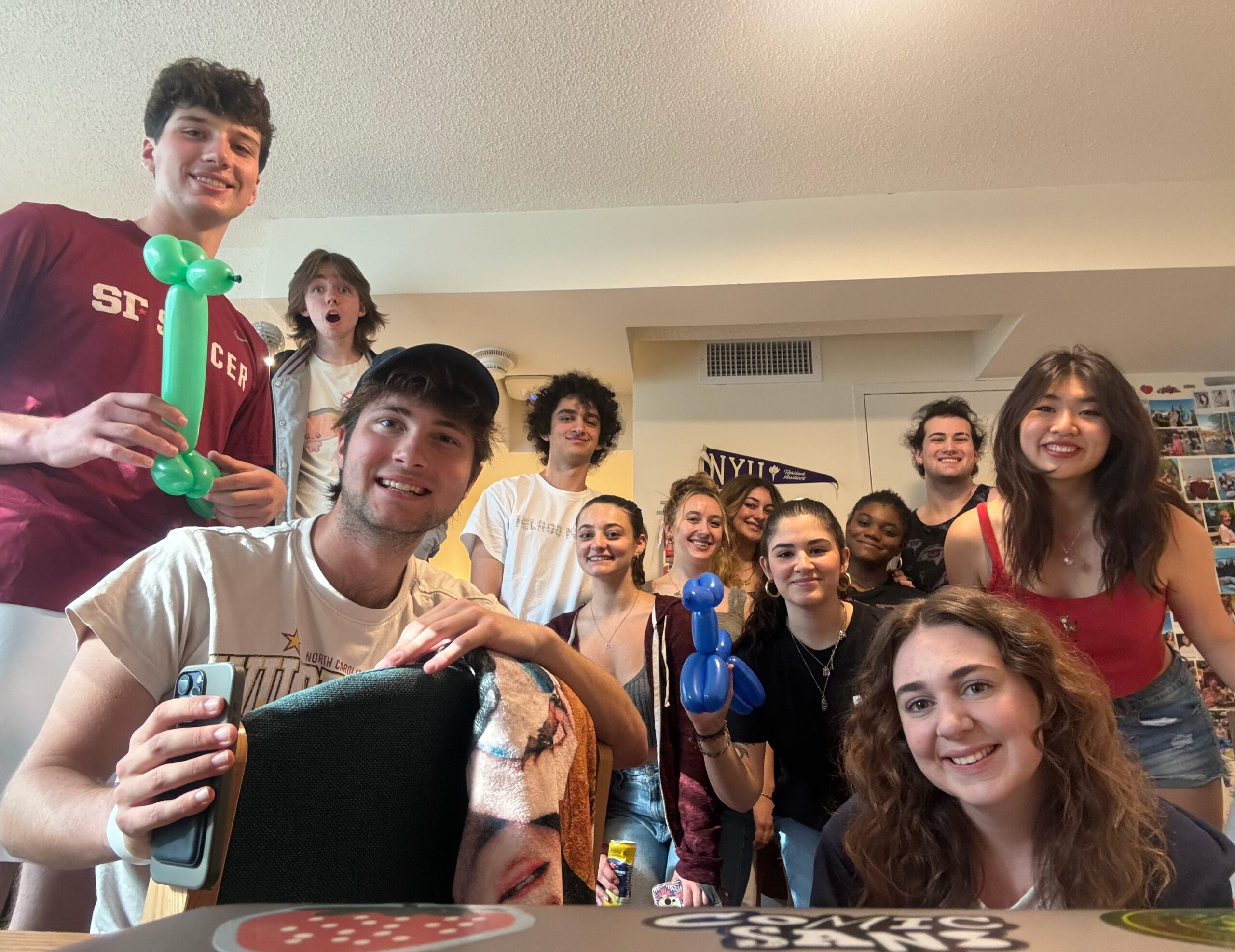 A large group of students posing together during a dorm hall event. A few of the students are holding balloon animals.