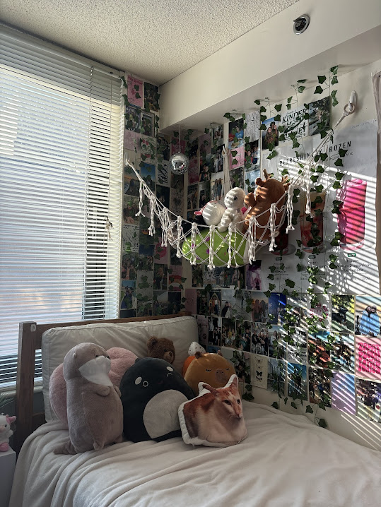 A dorm room with a photo wall, stuffed animals, and a disco ball on the wall