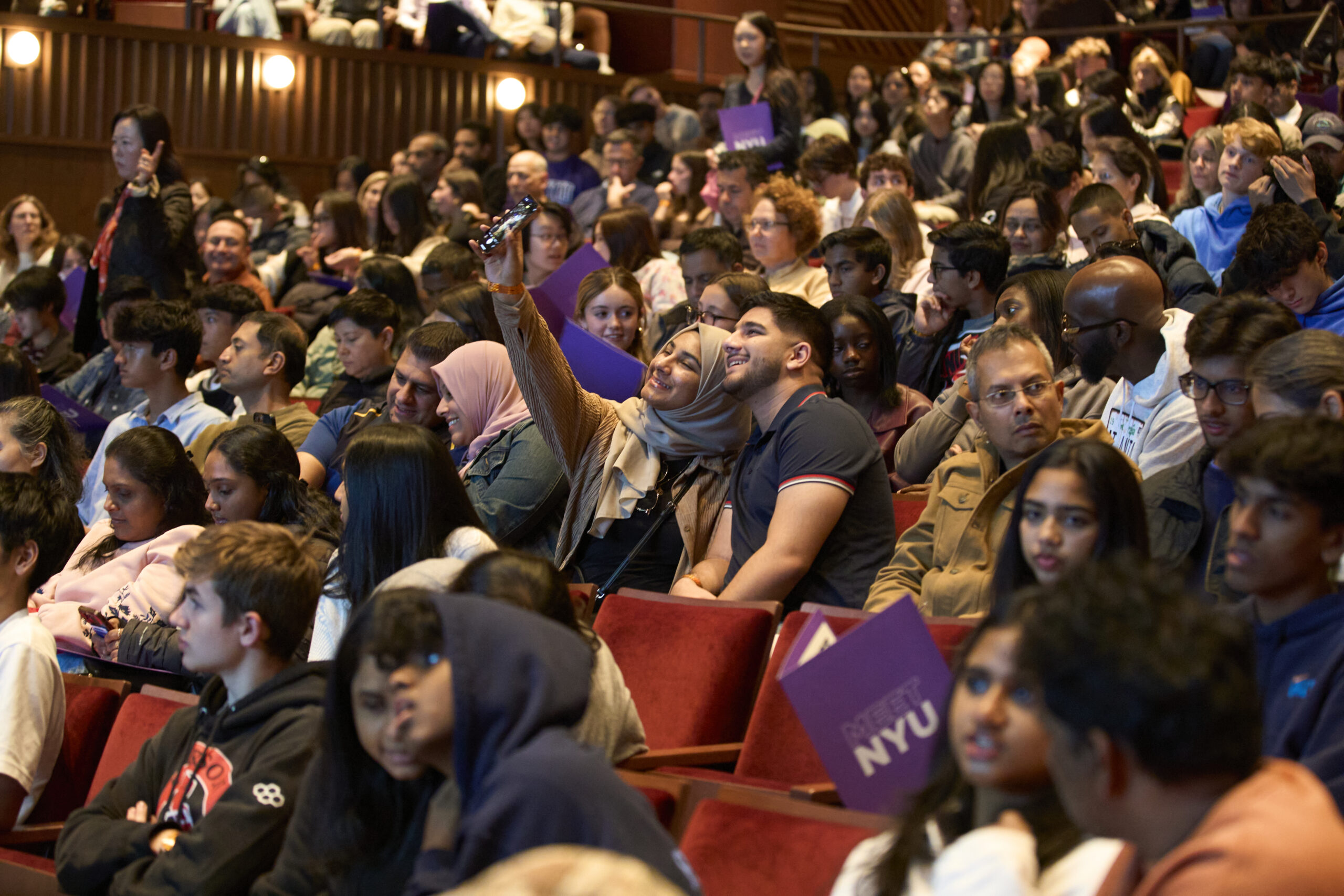 two students take a selfie in a crowded auditiorium of admitted students