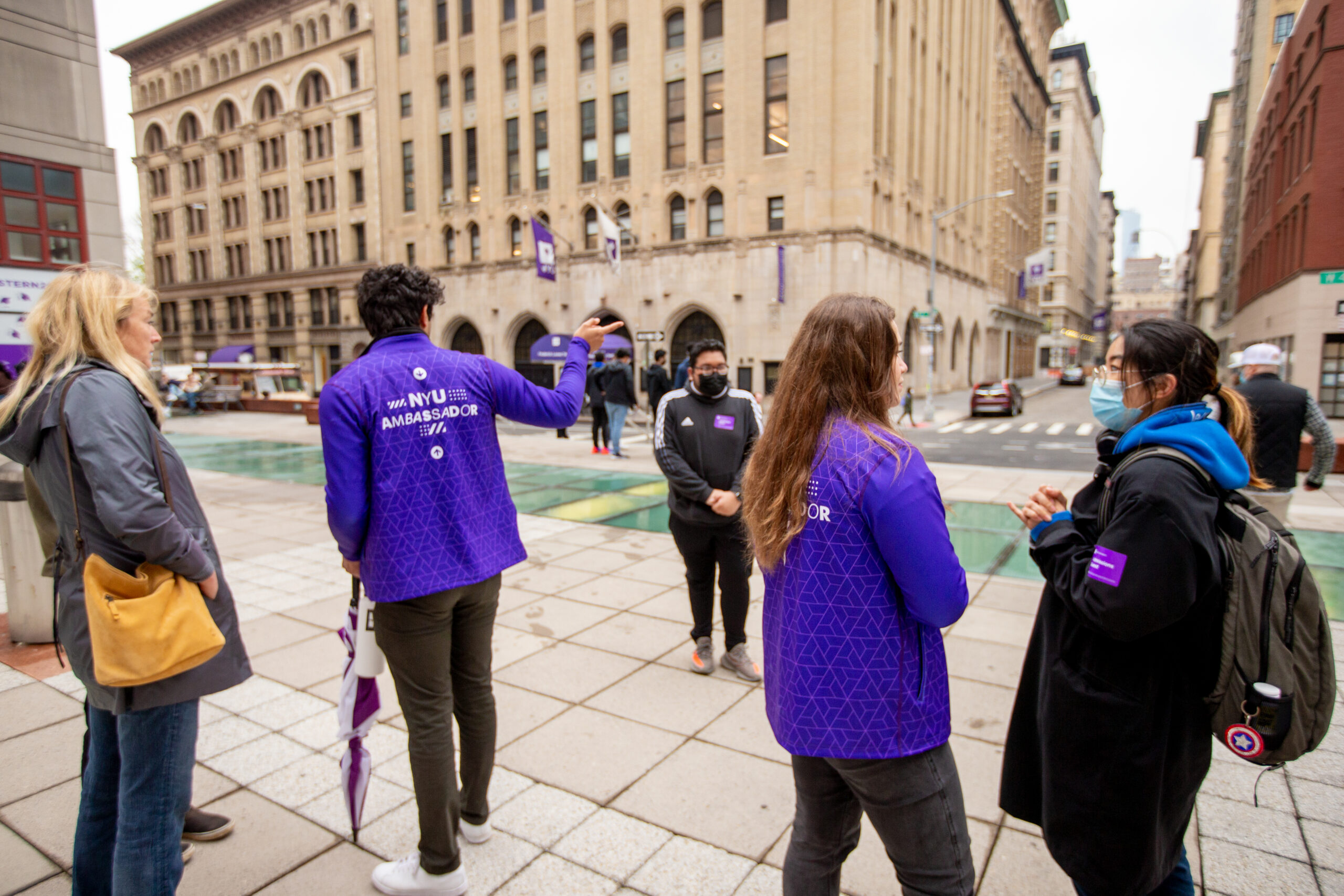 Two purple-clad student Admissions Ambassadors give guests directions on campus.