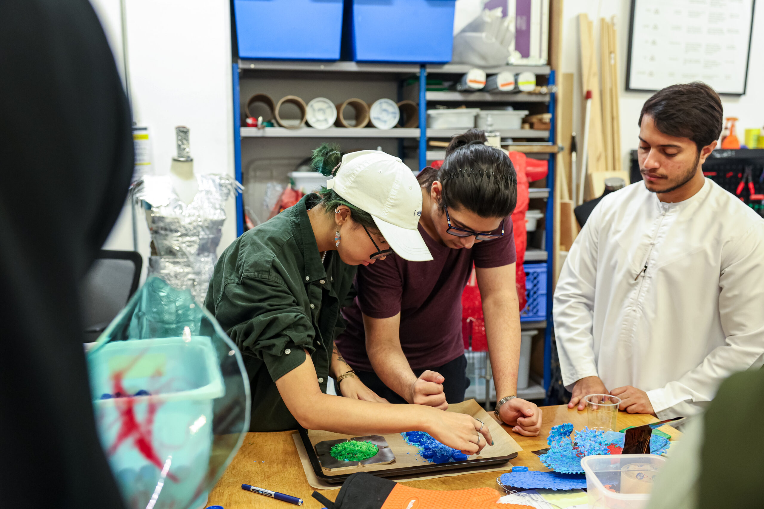 Students collaborating in the Plastics Lab at NYU Abu Dhabi, shaping pieces of recycled plastic on a workspace surrounded by materials.