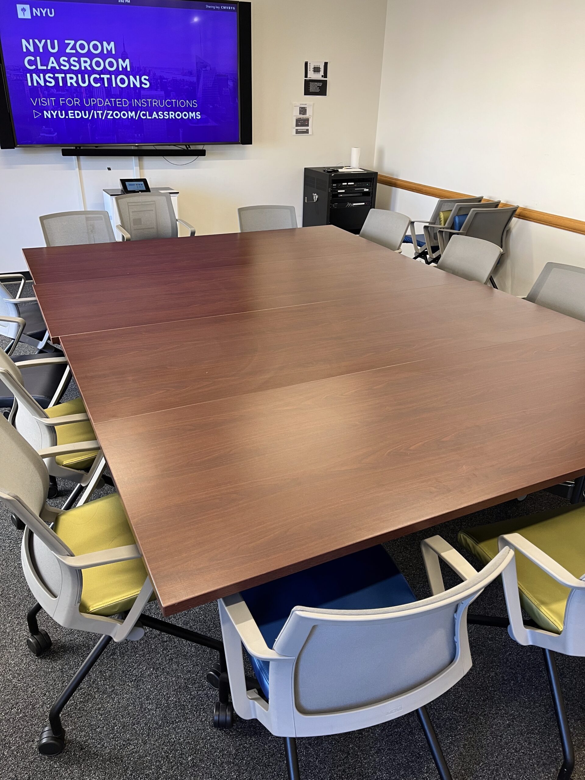 A bunch of chairs surrounding a large square table in a classroom.