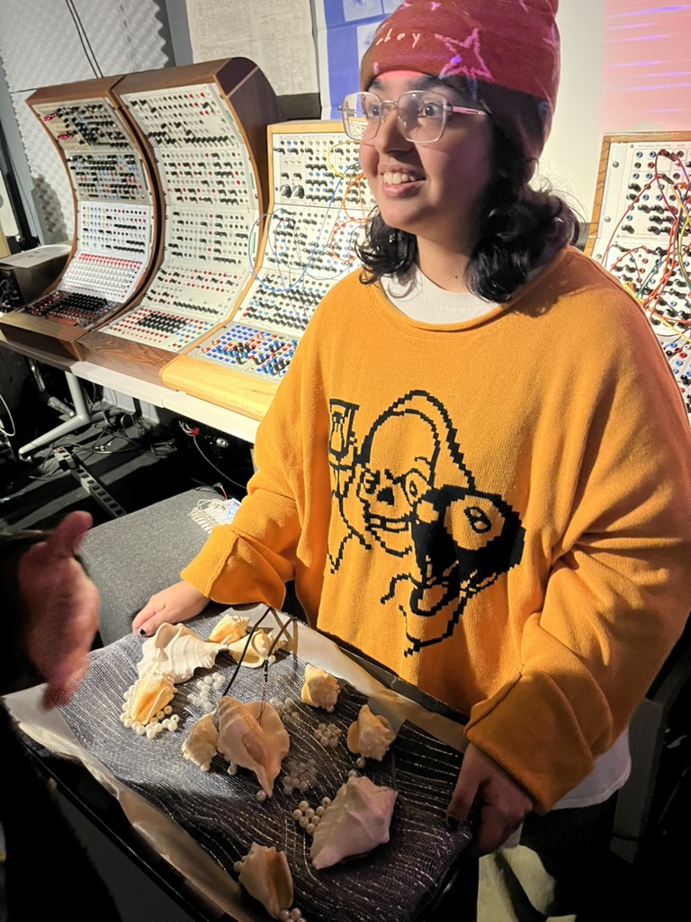 A student holds an engineering project made of seashells and sound equipment.