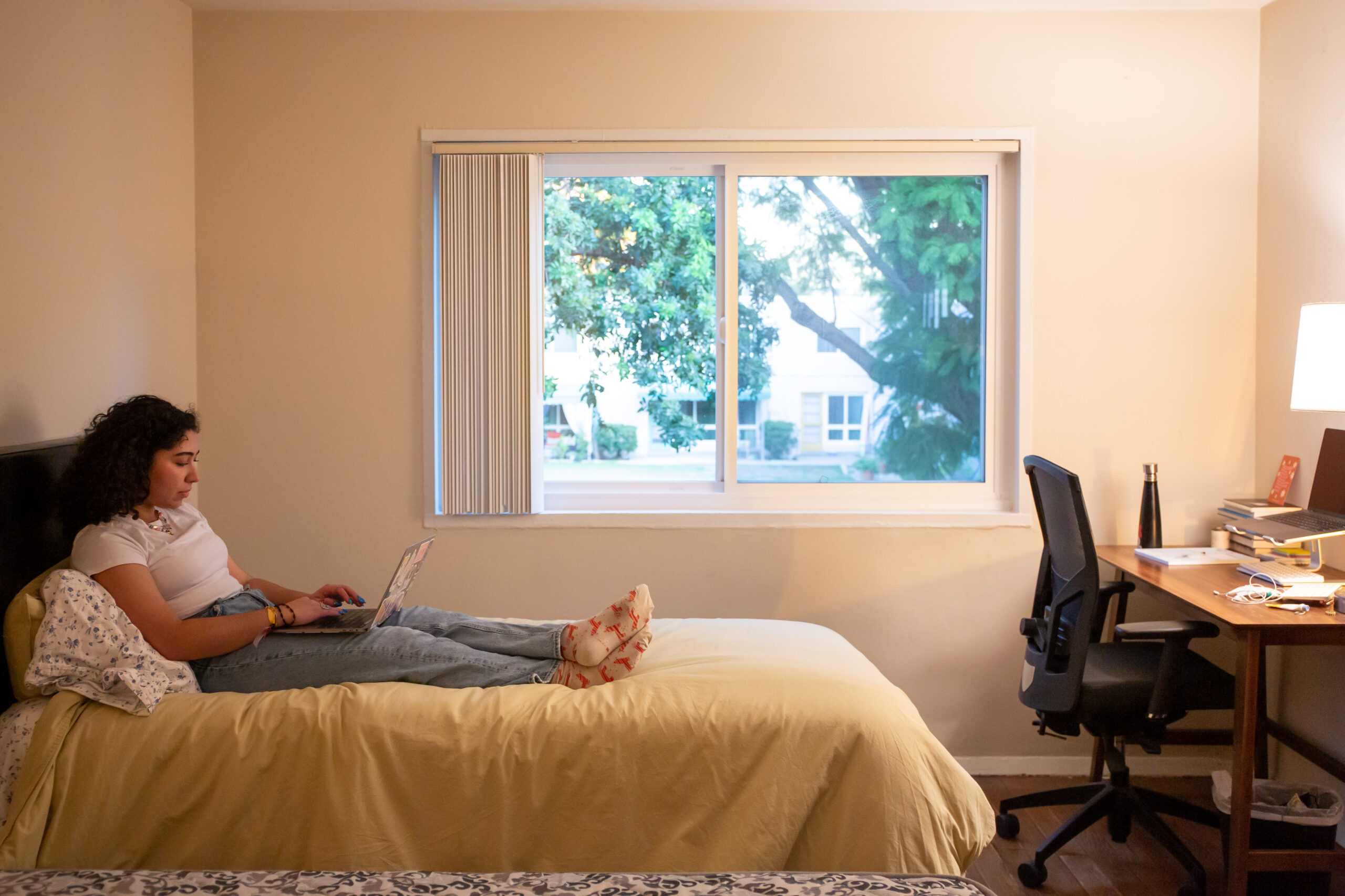 A student working on their laptop in bed.