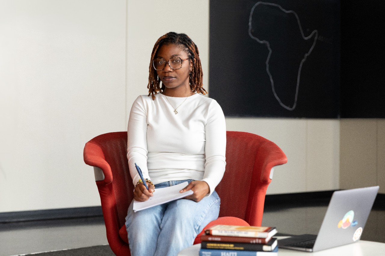 Portrait of Maame Adwoa Sey, seated in a large reading chair with a notepad on her lap.