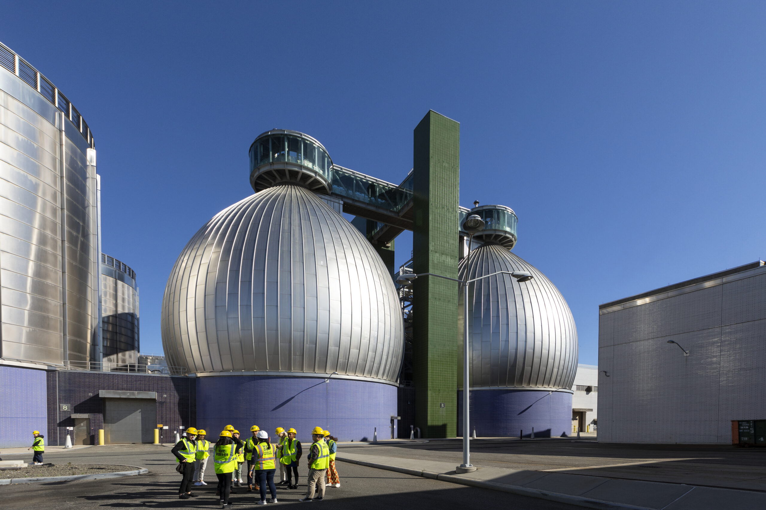A group of students in safety vests and hard hats tour a wastewater treatment facility.