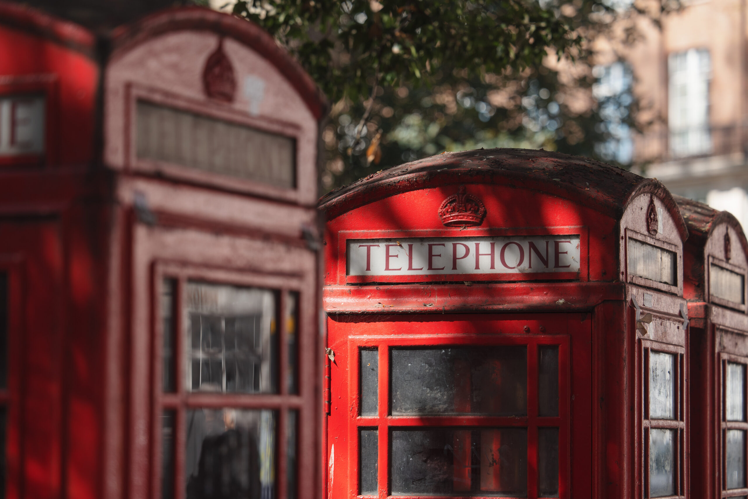 A close-up view of classic red British telephone booths, dappled shade falling across their worn surfaces.